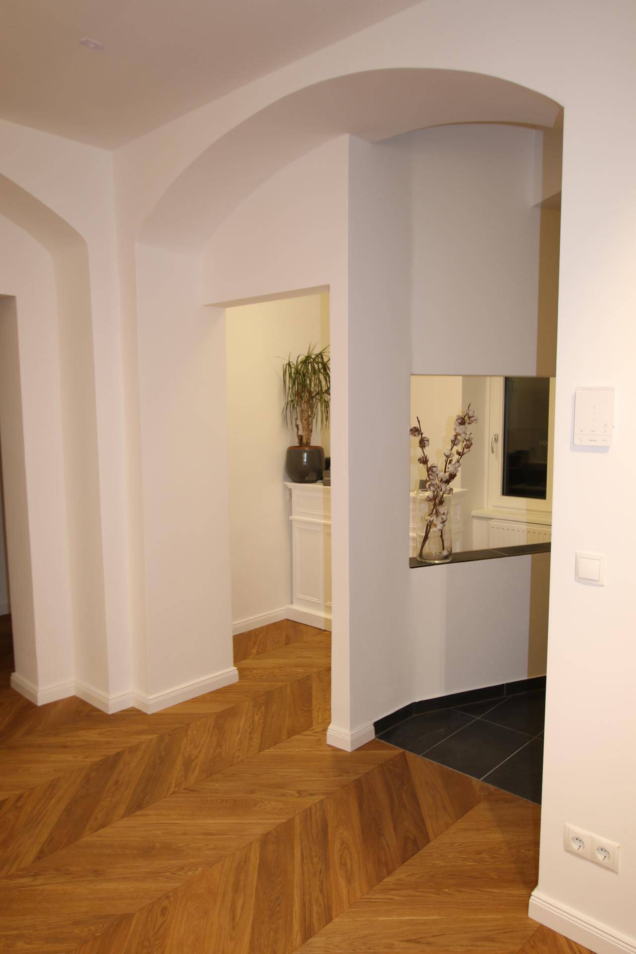 Heller Flur mit Fischgrätparkett und eleganten Rundbögen, der zu weiteren Räumen führt.