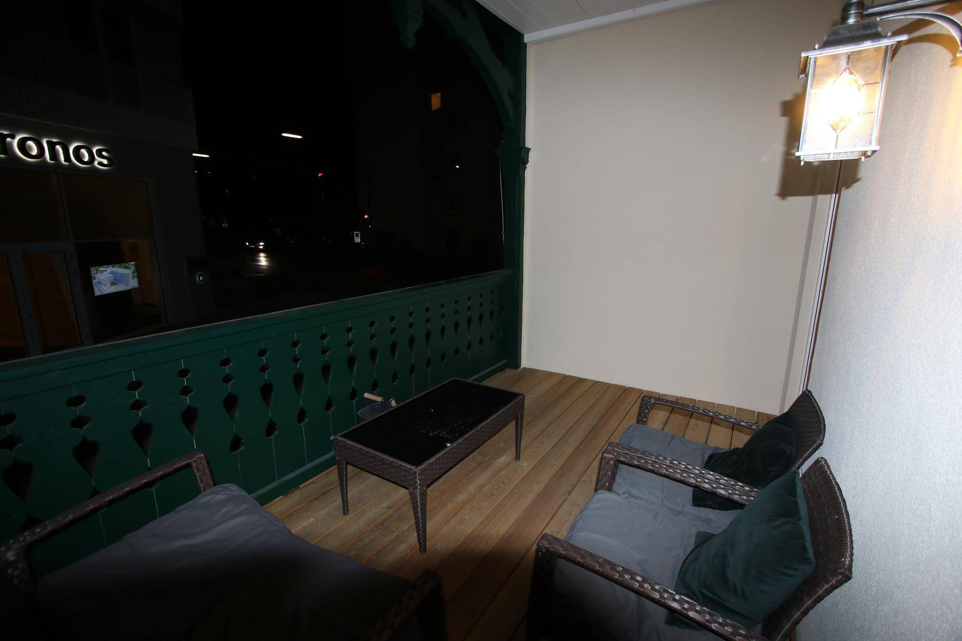 Balkon mit Korbmöbeln und Blick auf die Straße bei Nacht, beleuchtet von einer Lampe.