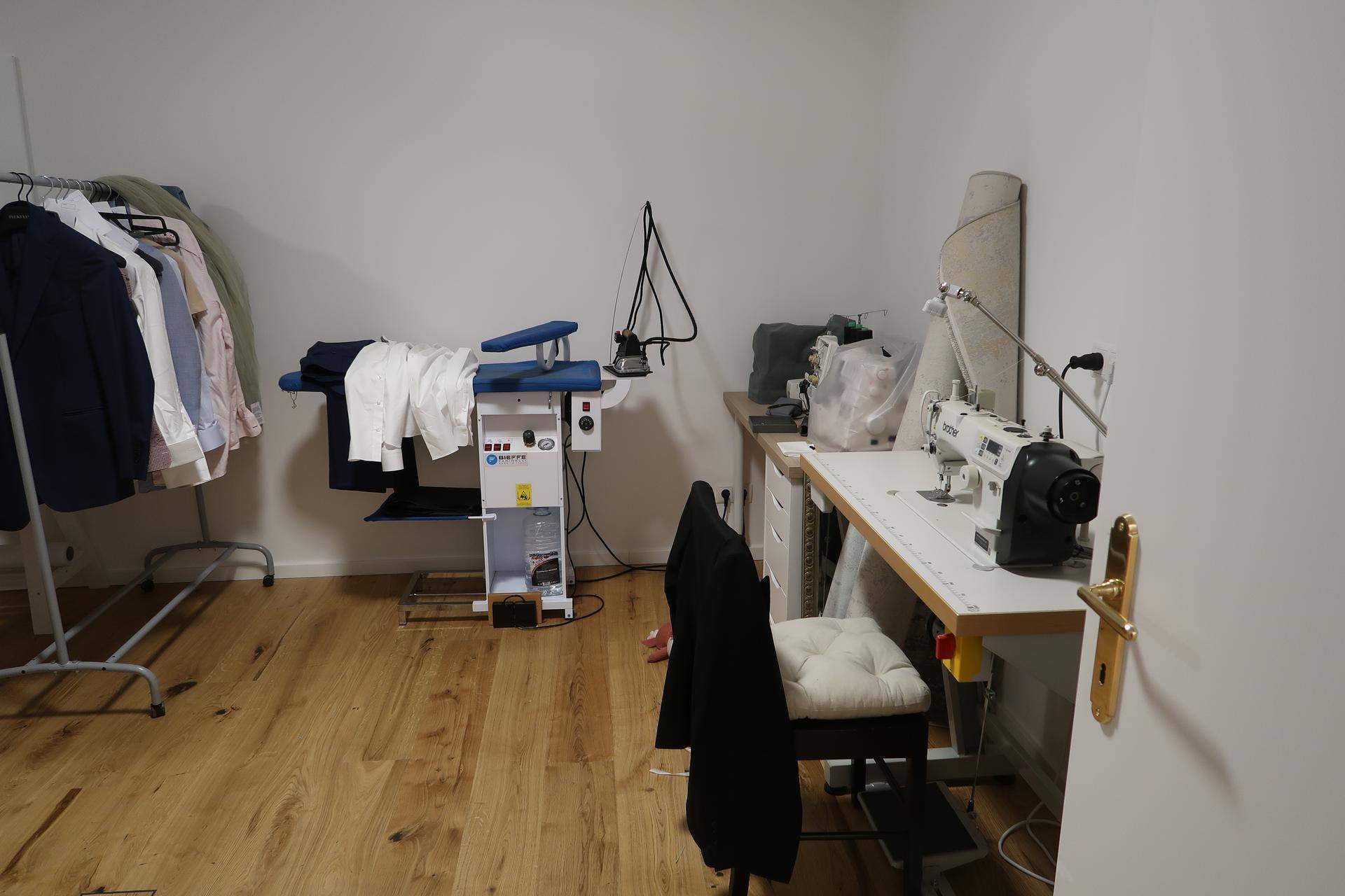 Werkstattraum mit Nähmaschinen, Bügelstation und Kleiderstange auf Holzfußboden.