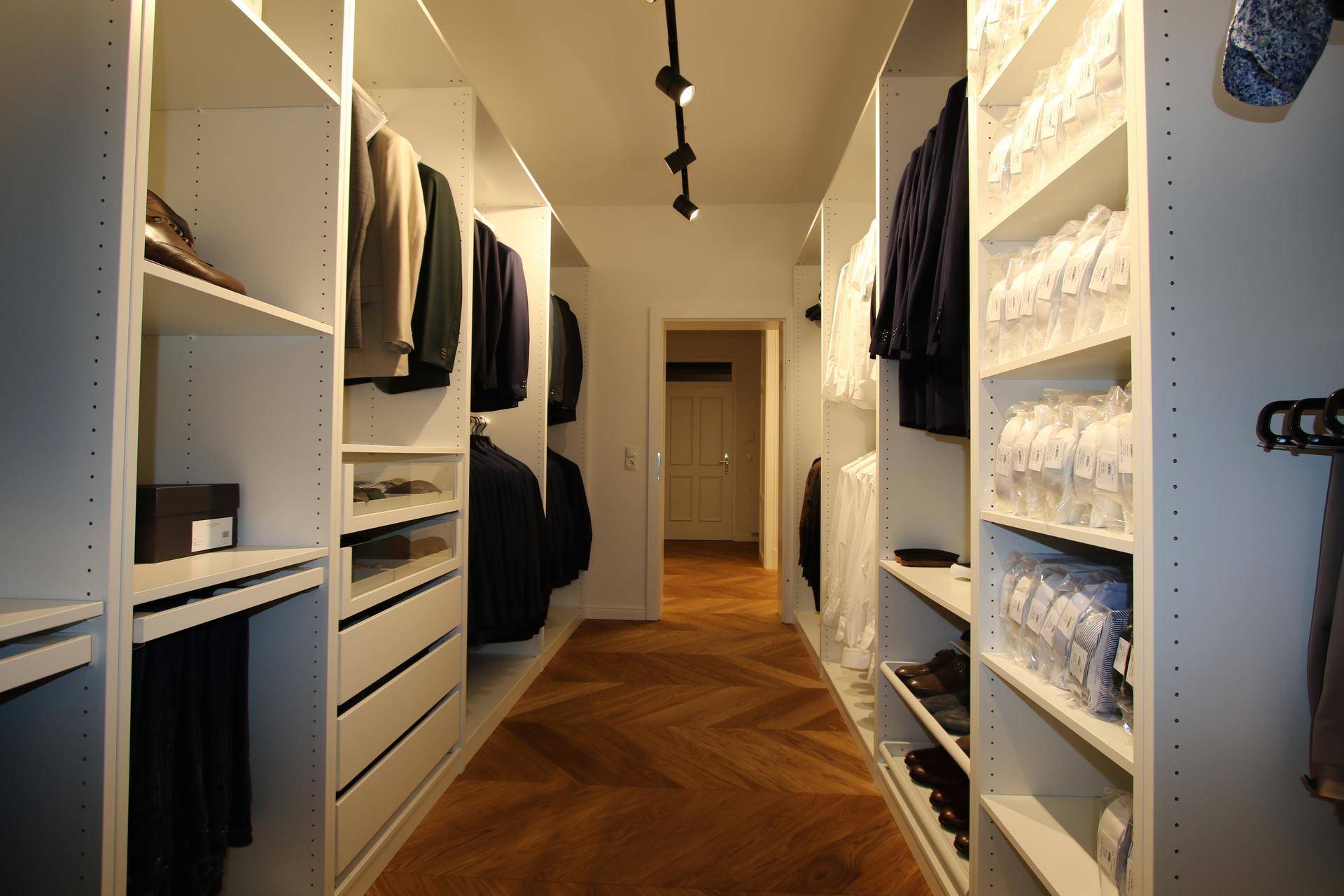 Geräumiger begehbarer Kleiderschrank mit vielen Regalen und Fischgrätparkett.