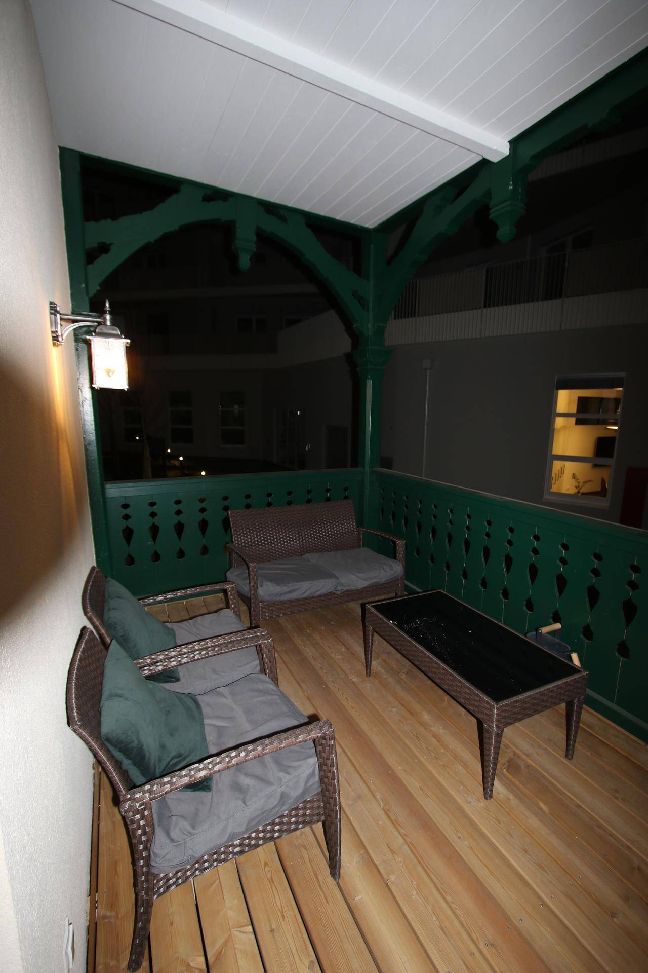 Gemütlicher Balkon am Abend mit Korbmöbeln und grüner Holzbrüstung.