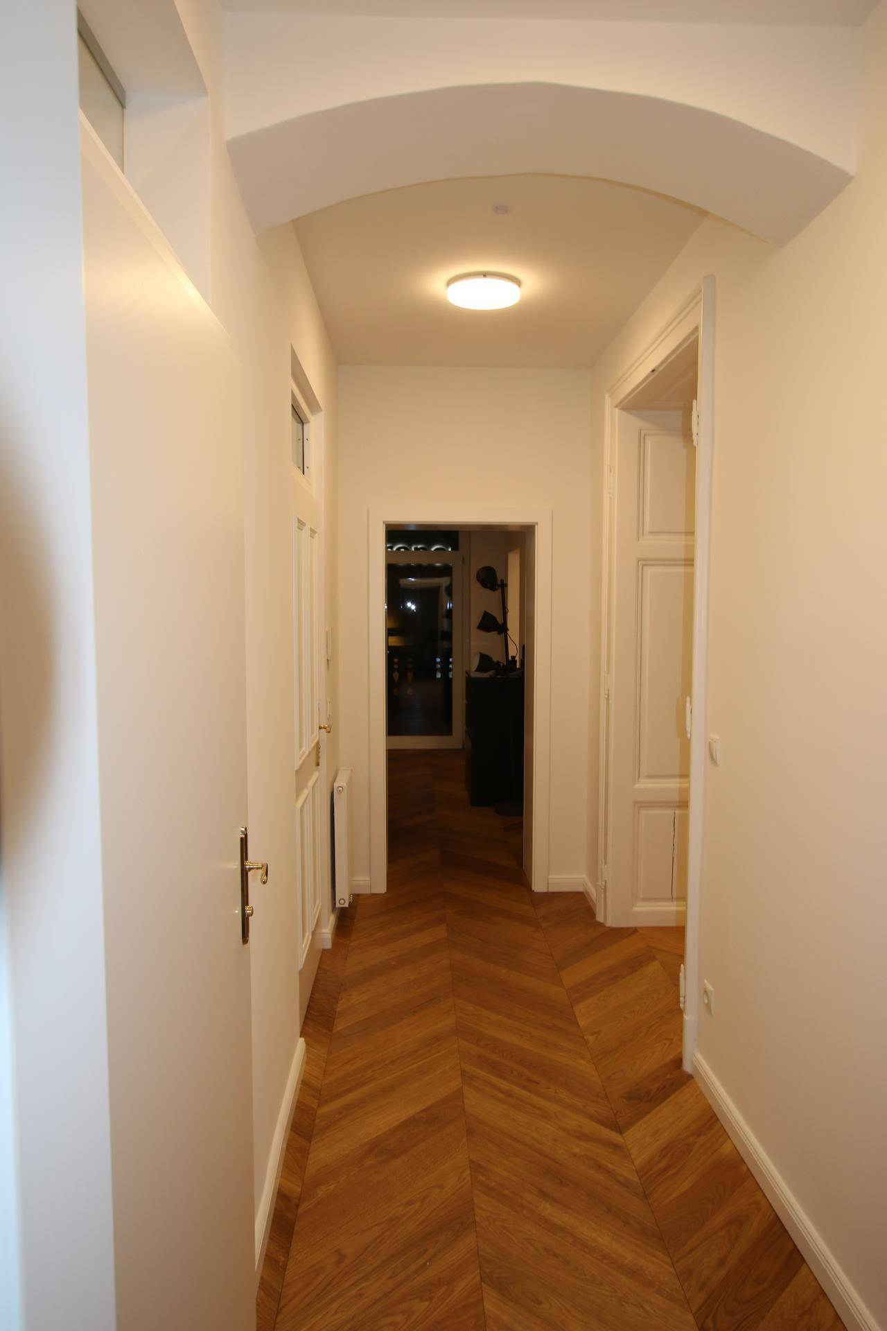 Langer Flur mit Fischgrätparkett, weißen Türen und einem eleganten Rundbogen.