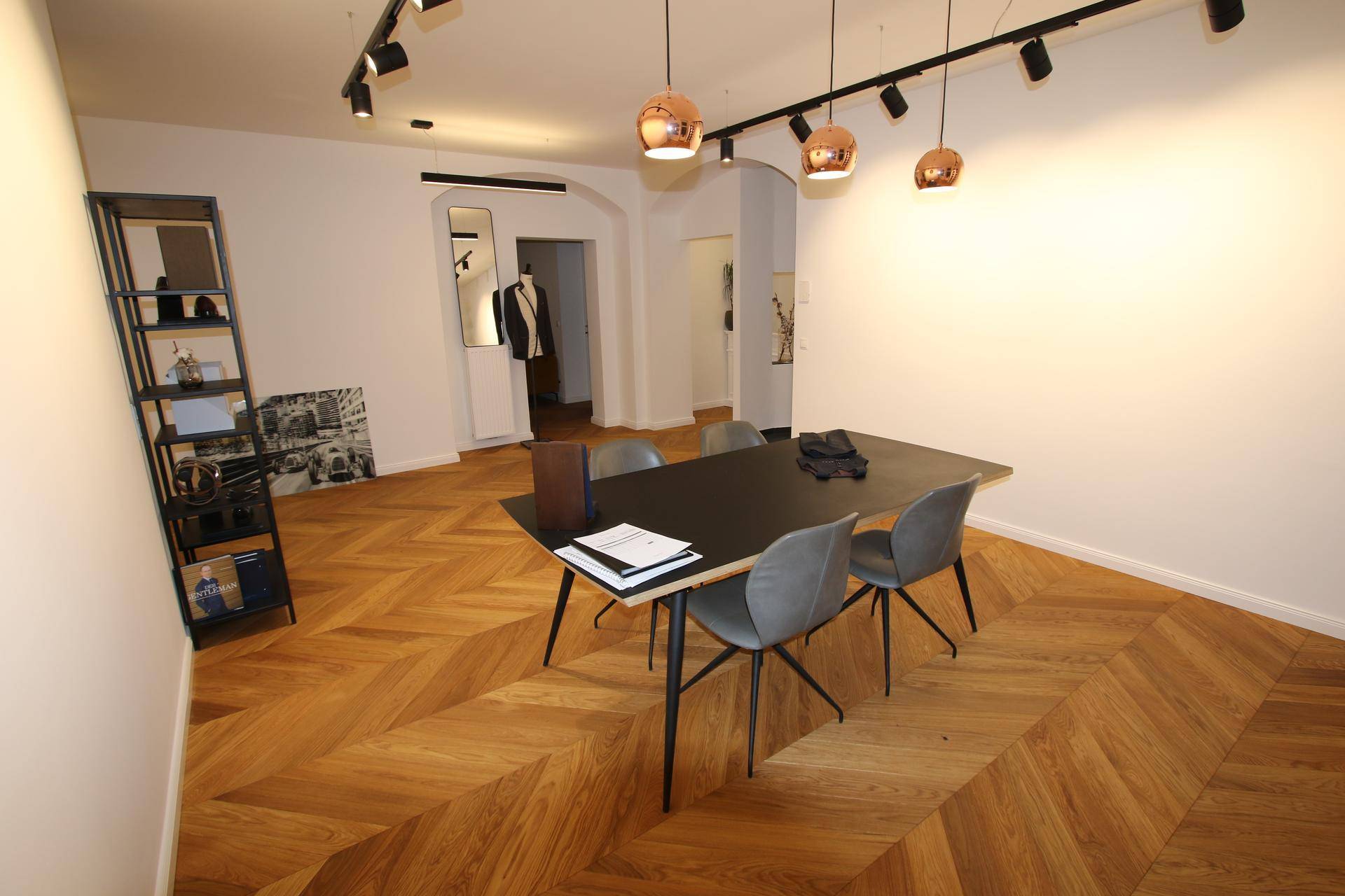 Moderner Bürobereich mit Fischgrätparkett, schwarzem Tisch und stilvollen Kupferlampen.