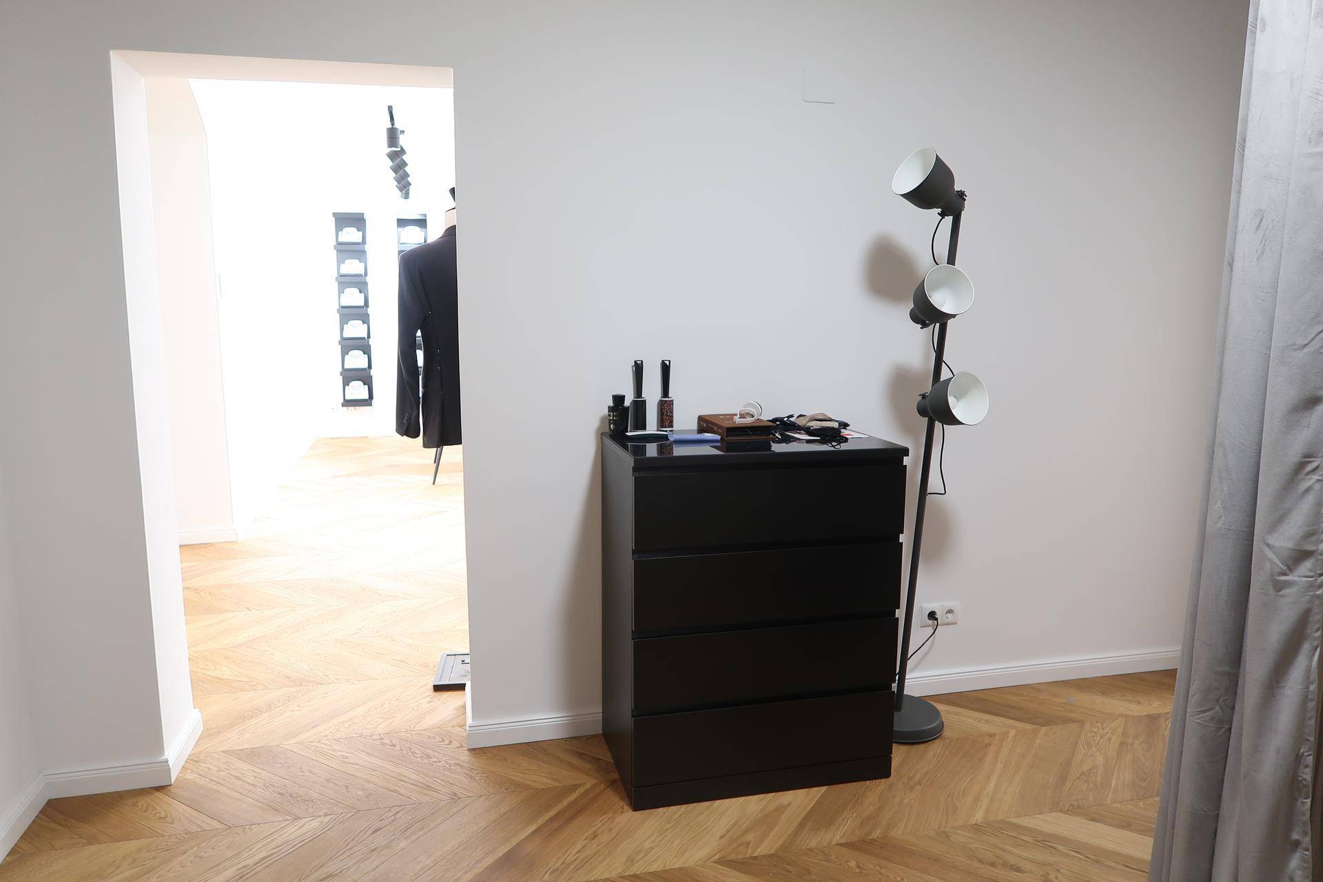 Ankleidebereich mit schwarzer Kommode, Stehlampe und Blick in einen weiteren Raum.