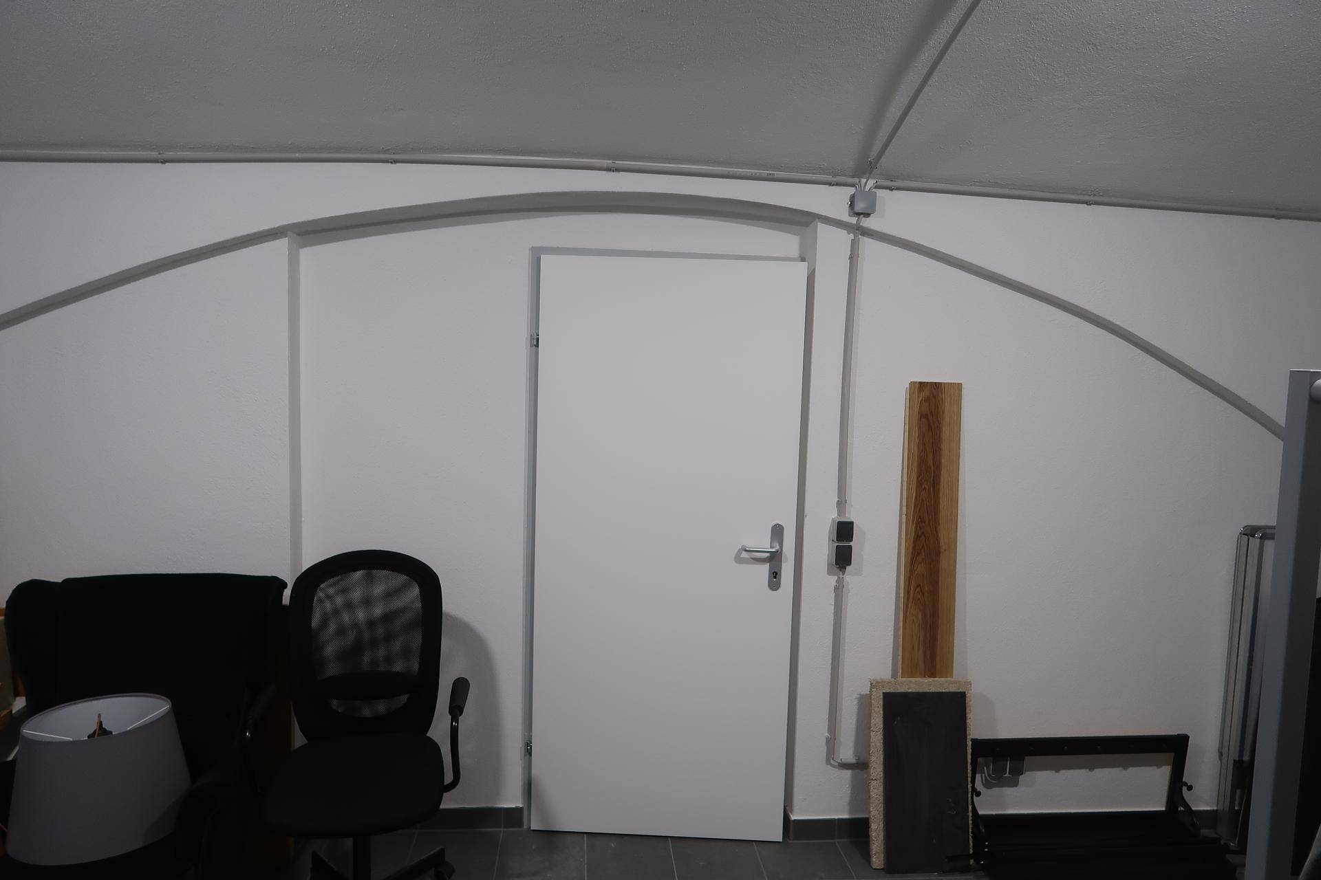 Geschlossene weiße Tür in einem Mehrzweckraum, umgeben von einer dekorativen Bogenstruktur an der Wand.