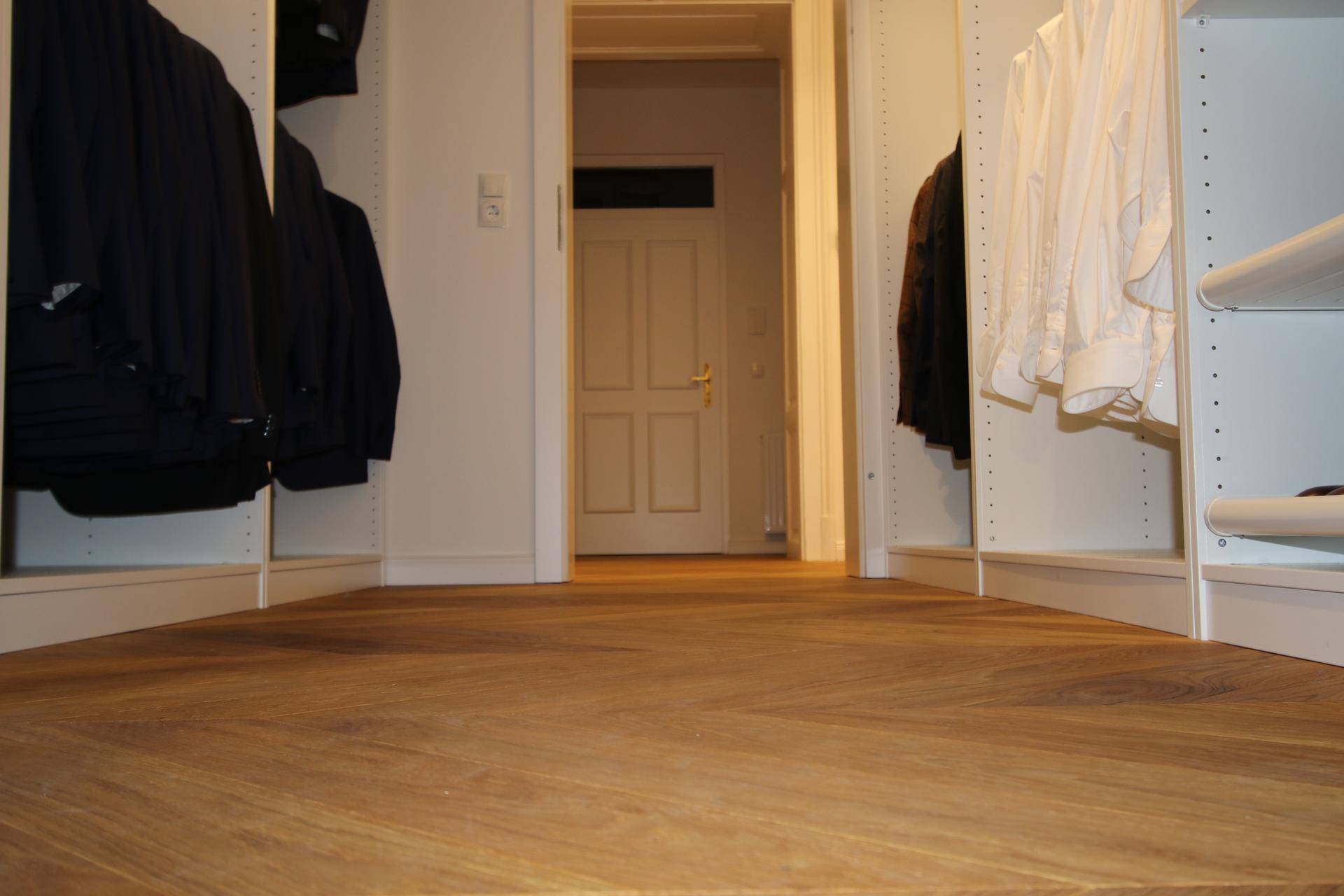 Blick vom begehbaren Kleiderschrank durch eine Tür in einen hellen Flur.