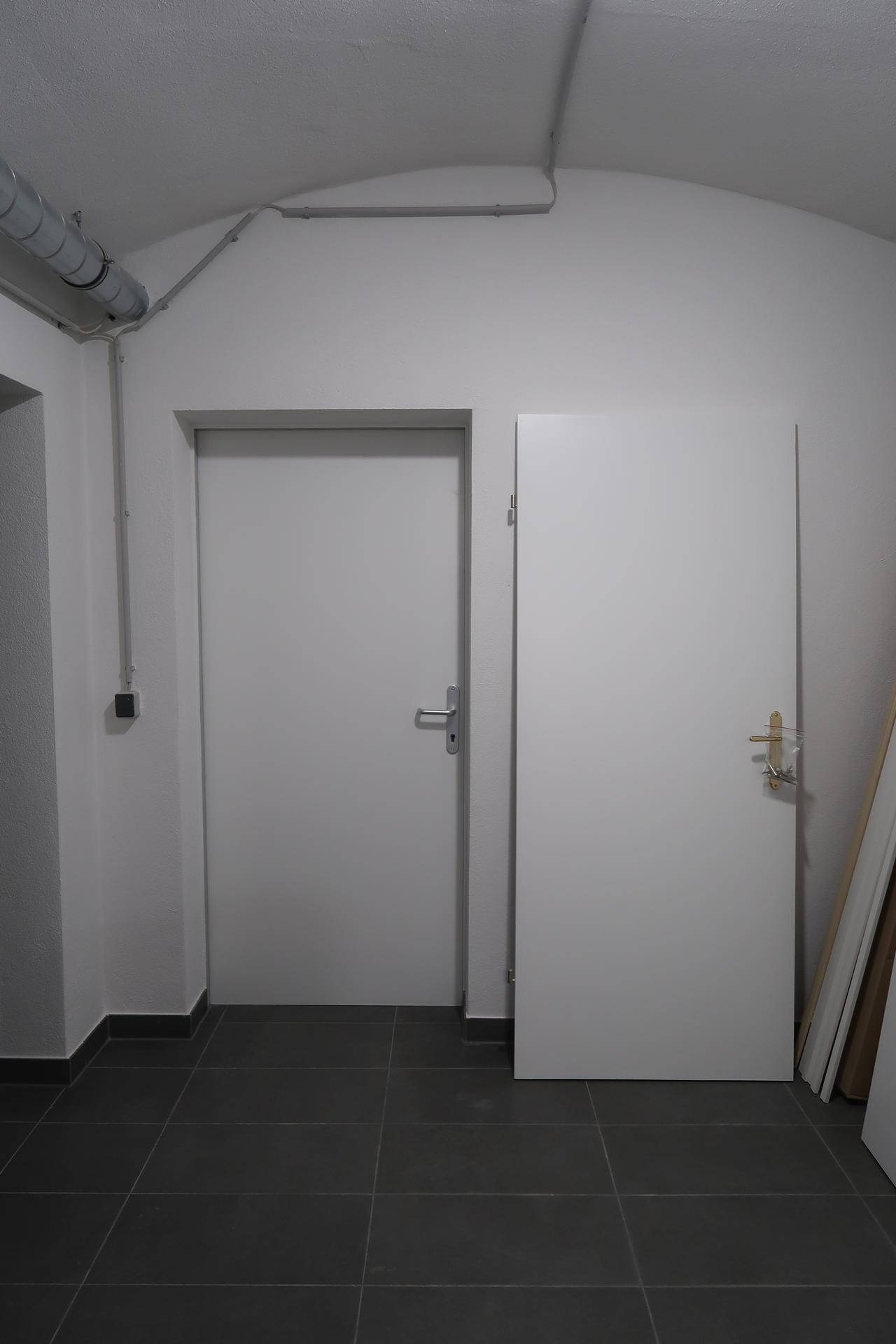 Zwei schlichte weiße Türen in einem Flur mit grauem Fliesenboden und einer gewölbten Decke.