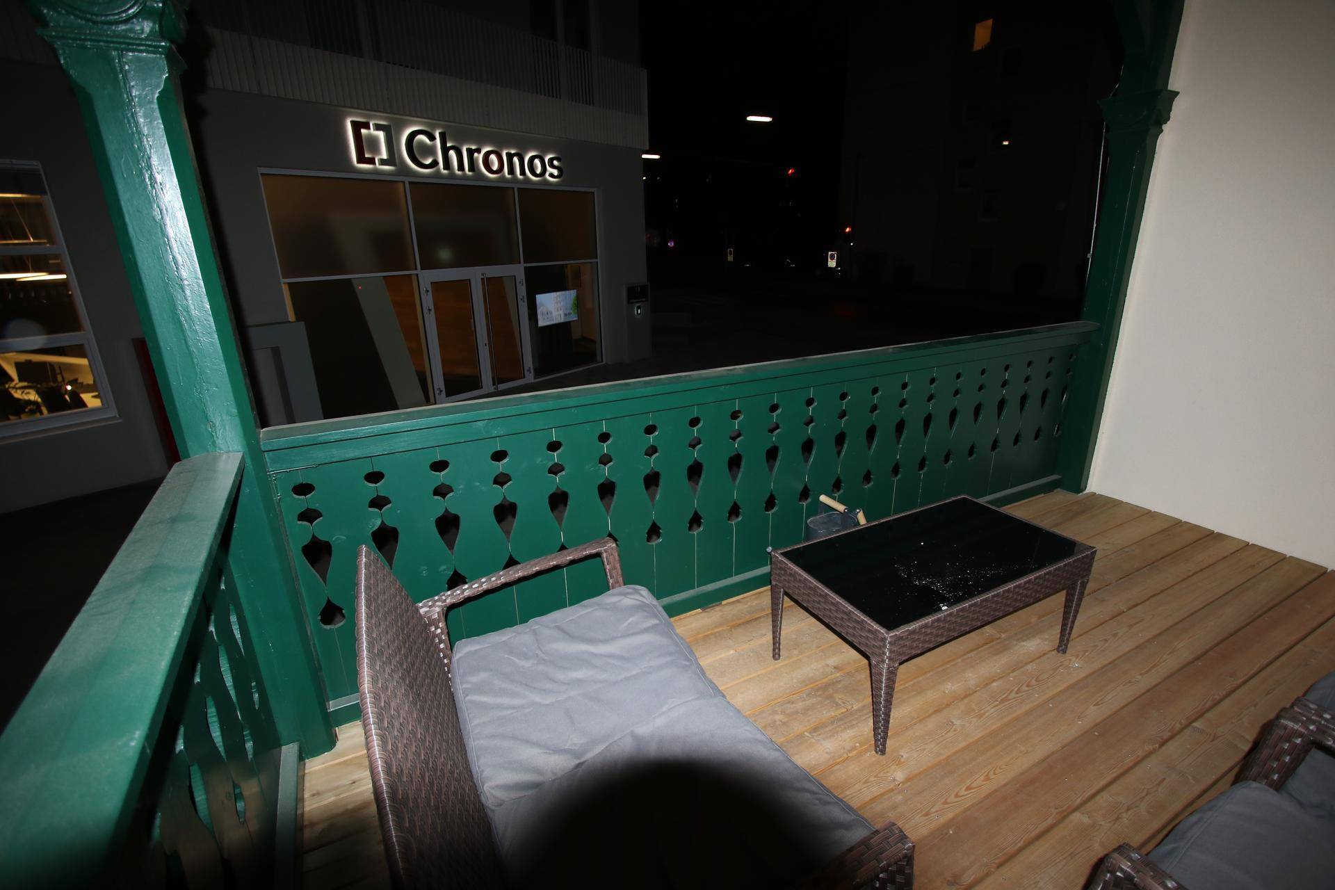 Balkon mit grüner Holzbrüstung und Blick auf ein Gebäude mit der Aufschrift "Chronos".