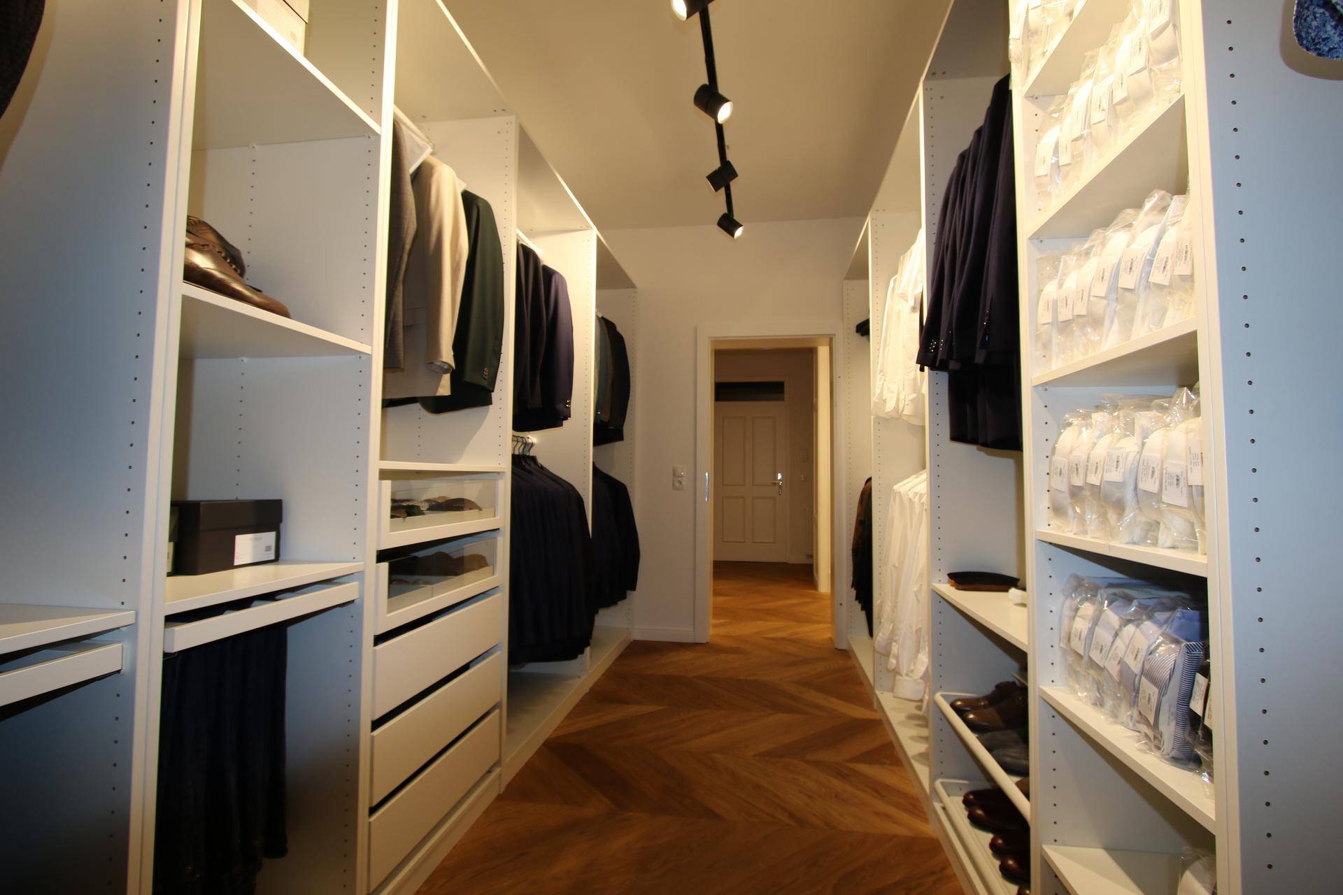 Begehbarer Kleiderschrank mit weißen Regalsystemen und elegantem Fischgrätparkett.