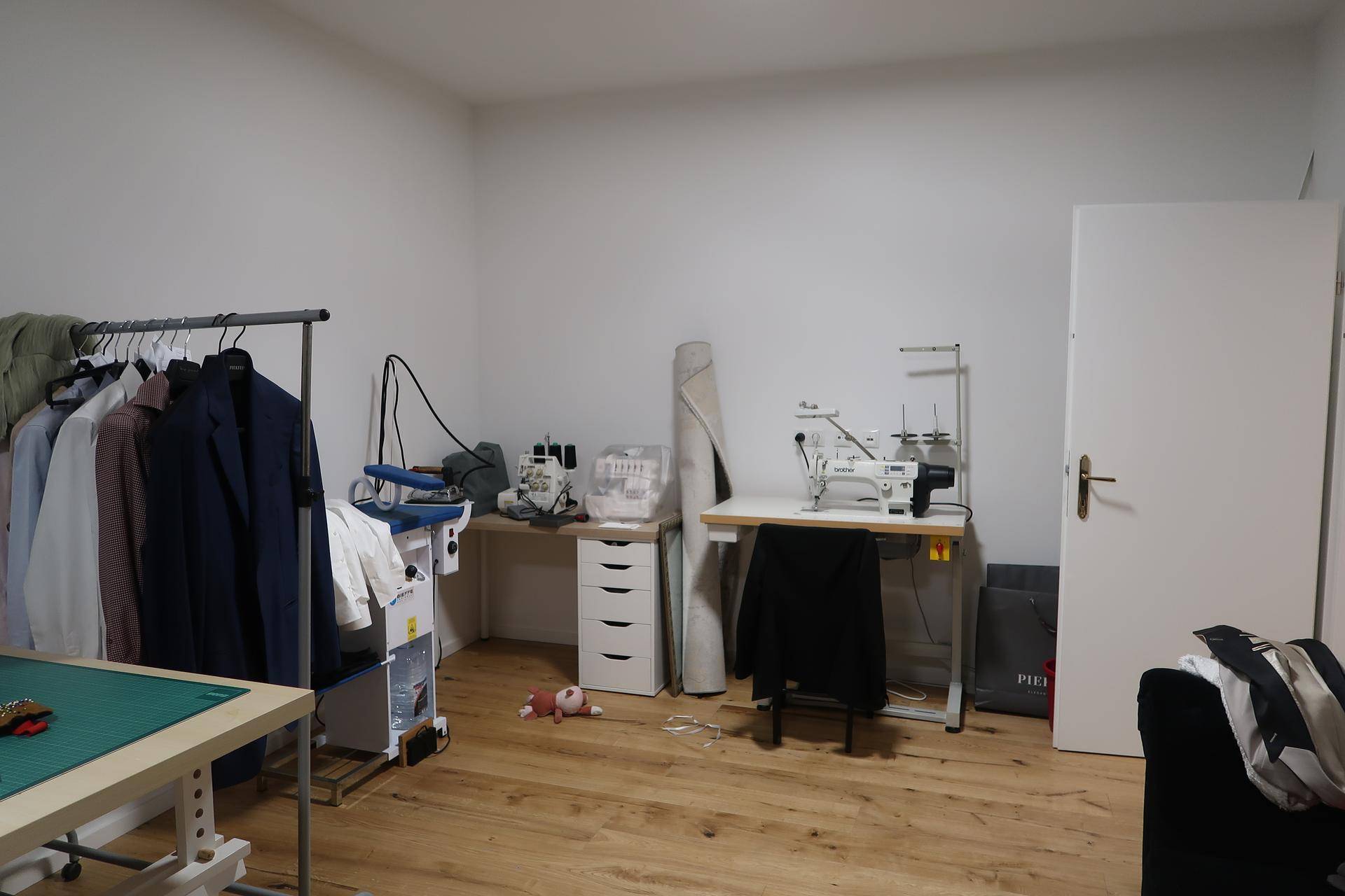 Werkstattraum mit Nähmaschinen, Bügelstation und Kleiderstange auf Holzfußboden.