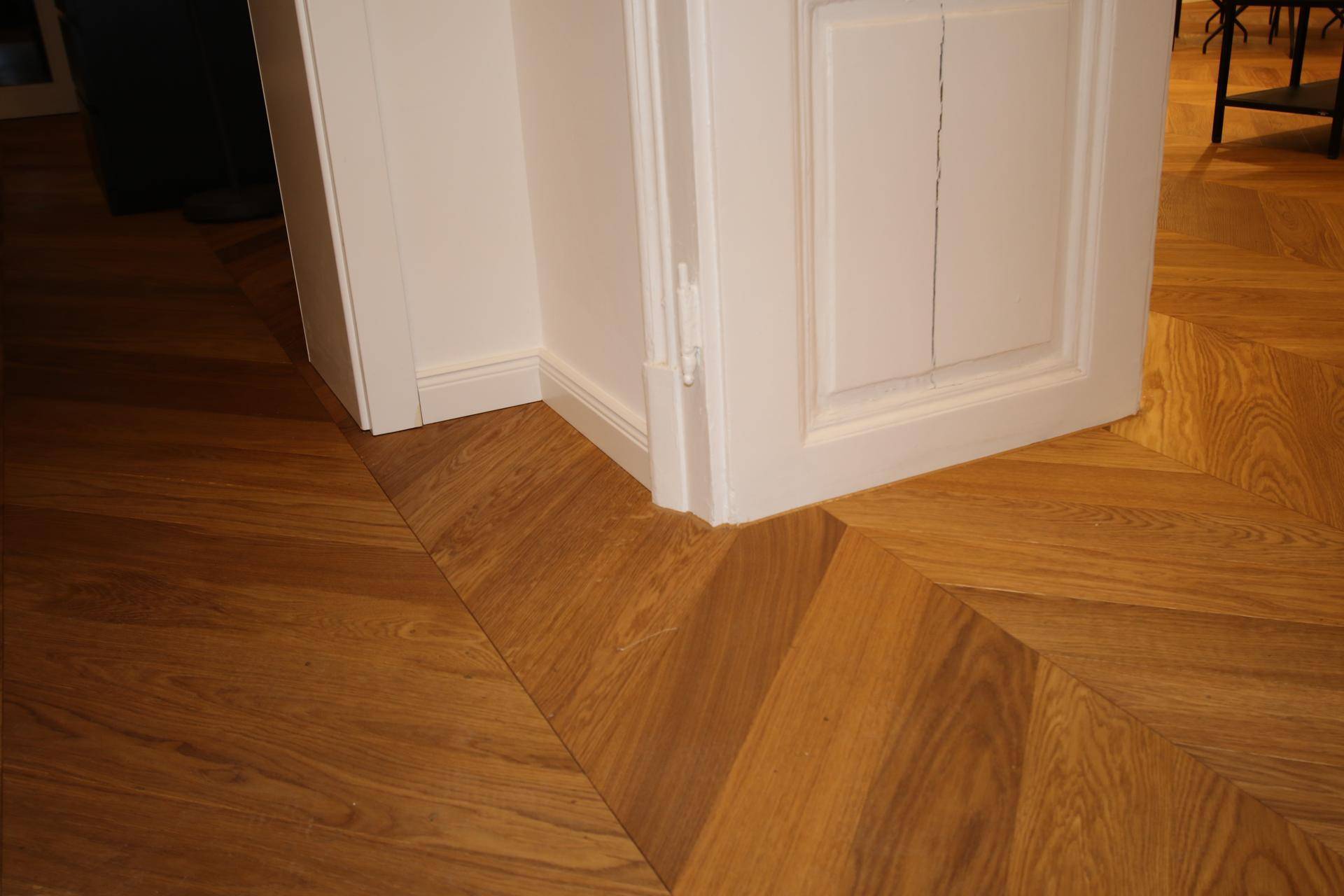 Detailaufnahme des Fischgrätparketts im Flur, das sich elegant um den Türrahmen legt.