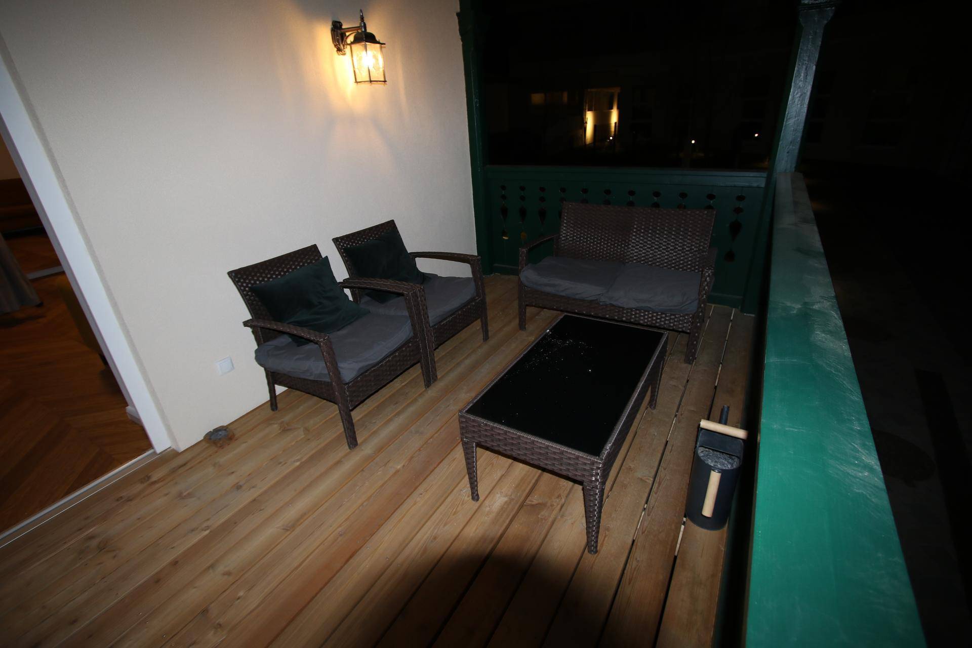 Balkon mit Korbmöbeln und einem kleinen Tisch, beleuchtet von einer Wandlampe.
