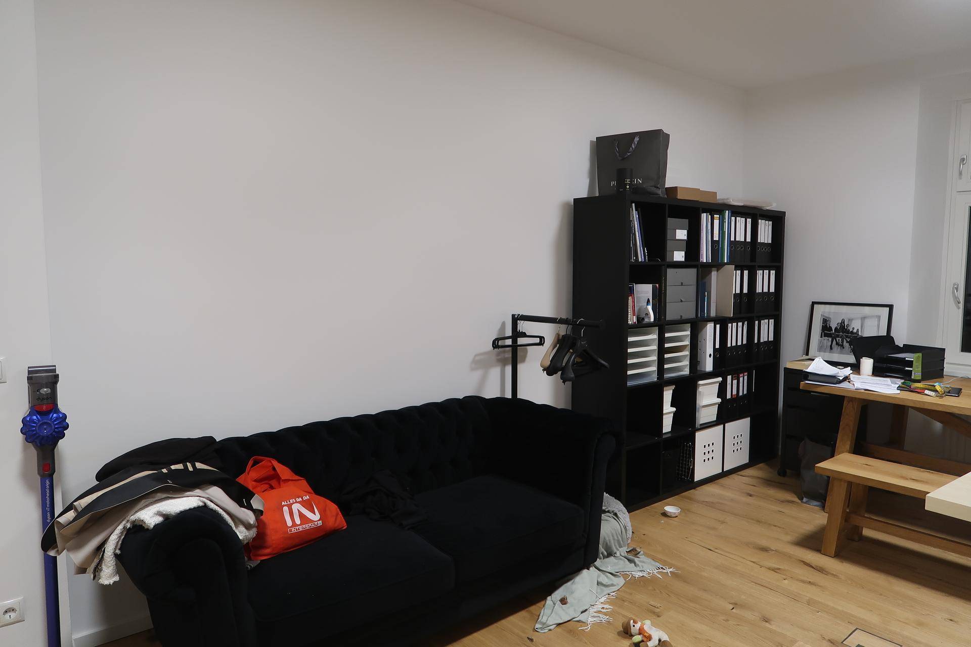 Arbeitszimmer mit schwarzem Sofa, Regal und Holztisch auf Fischgrätparkett.