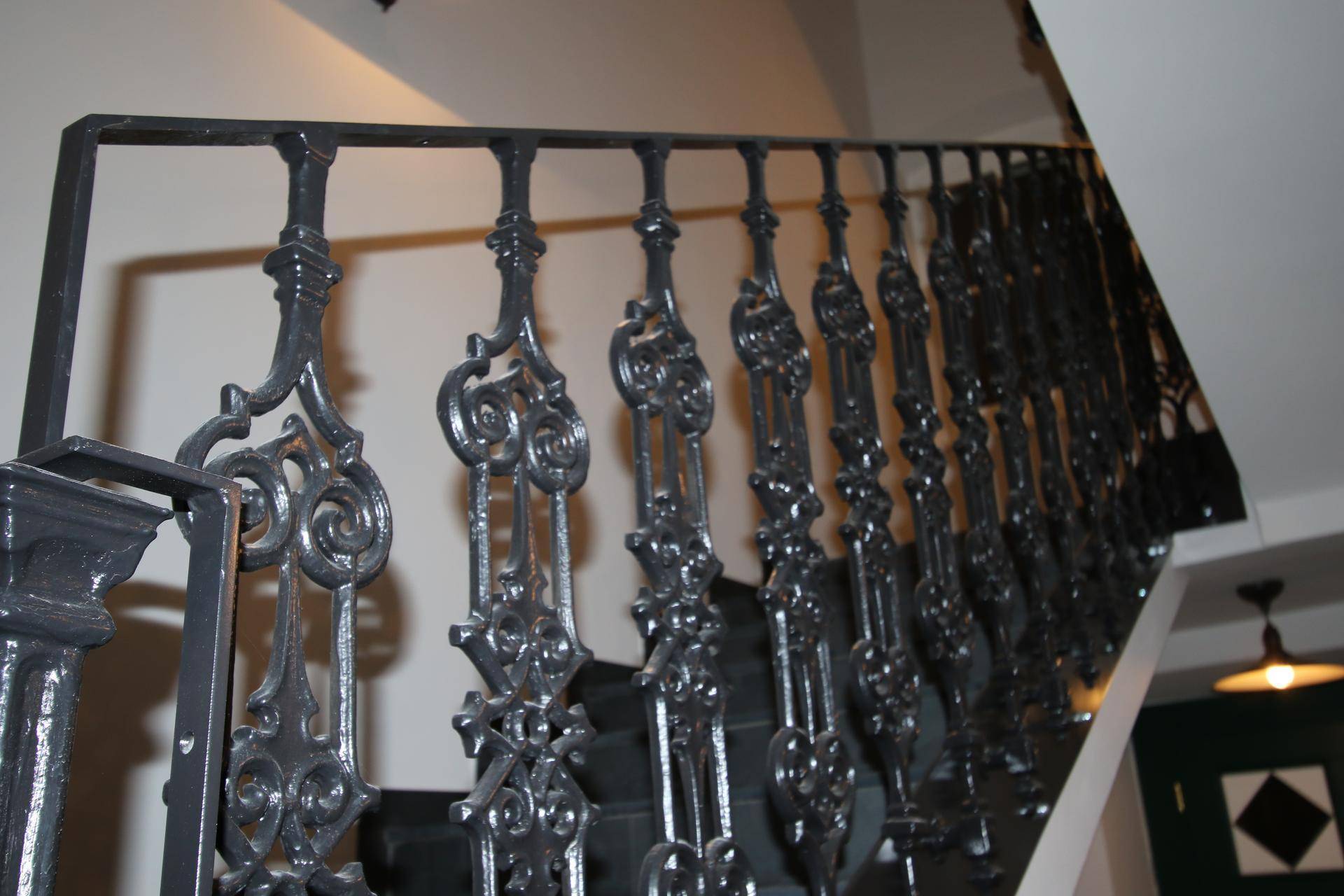 Detailaufnahme des kunstvoll geschmiedeten Treppengeländers in dunklem Metall.