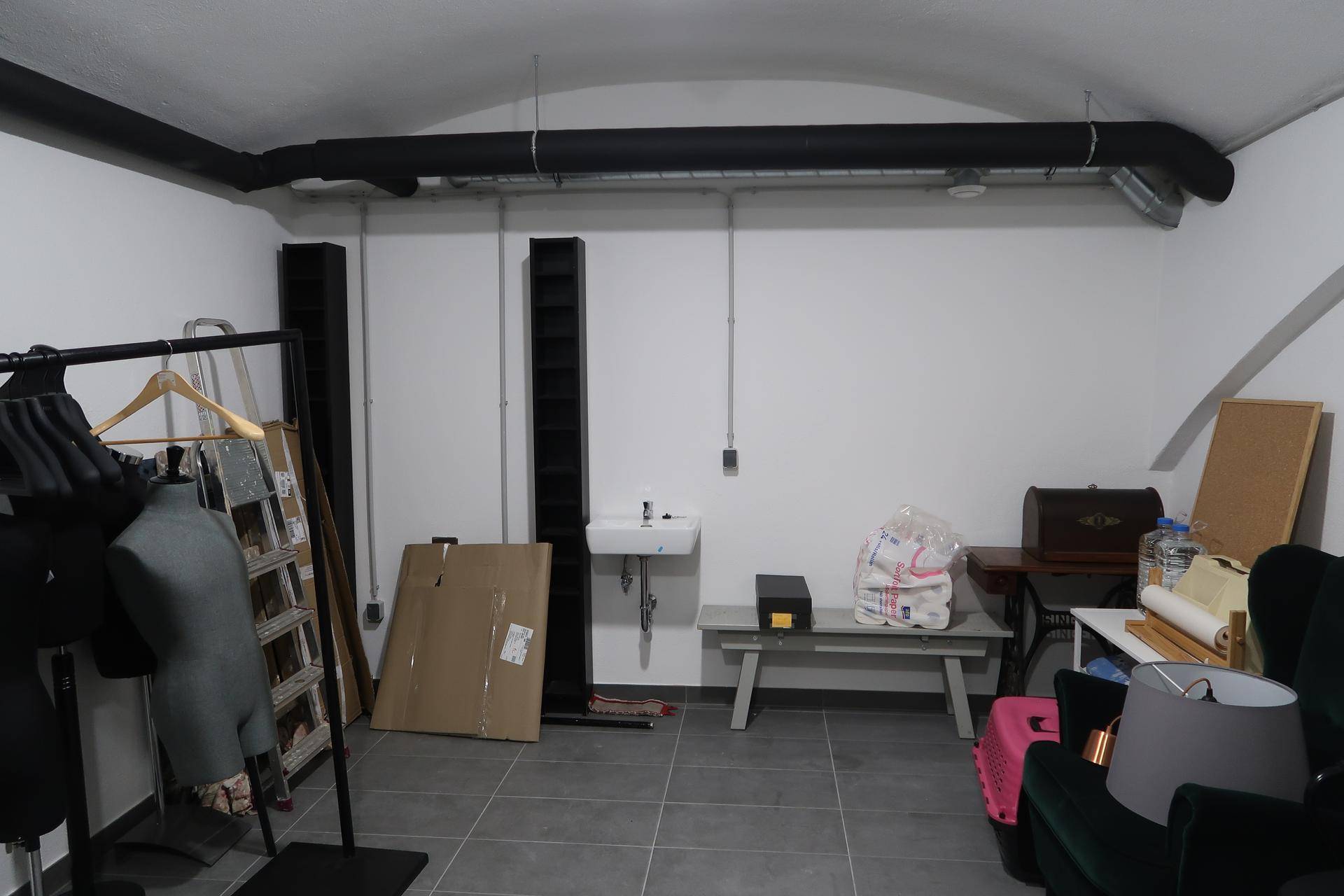 Mehrzweckraum mit kleinem Waschbecken, Kleiderständer und verschiedenen Gegenständen, unter einer gewölbten Decke.