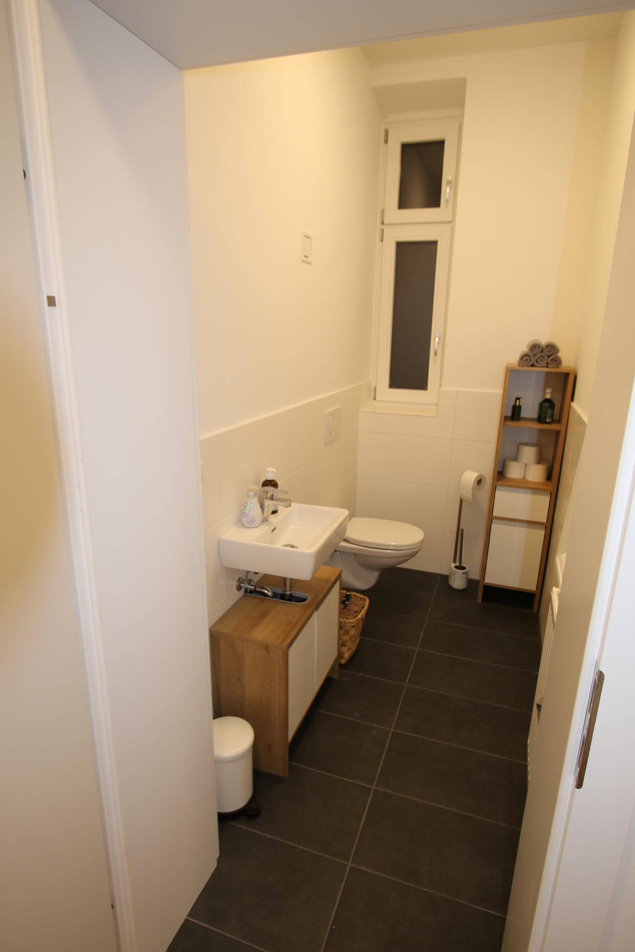 Modernes Gäste-WC mit dunklen Fliesen, kleinem Waschbecken und Fenster für Tageslicht.