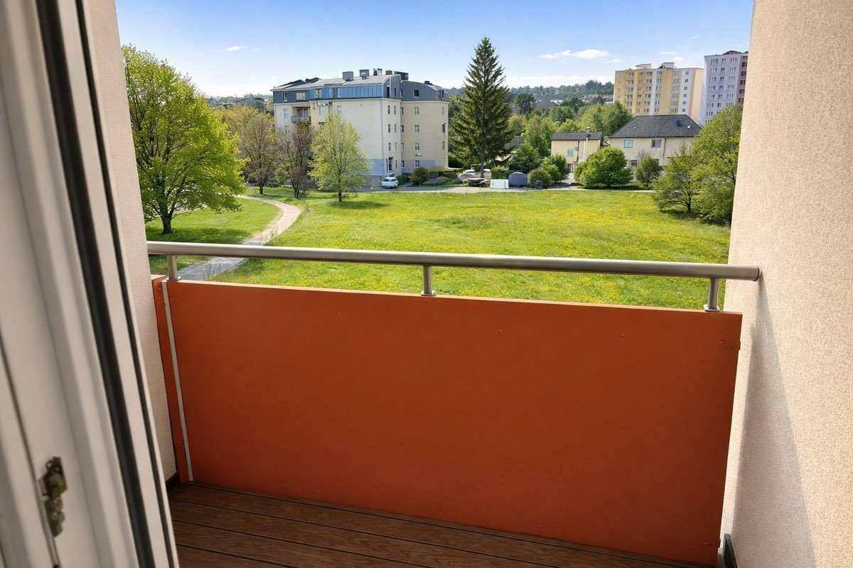 Balkon mit orangefarbener Brüstung und weitem Blick ins Grüne und auf umliegende Gebäude.