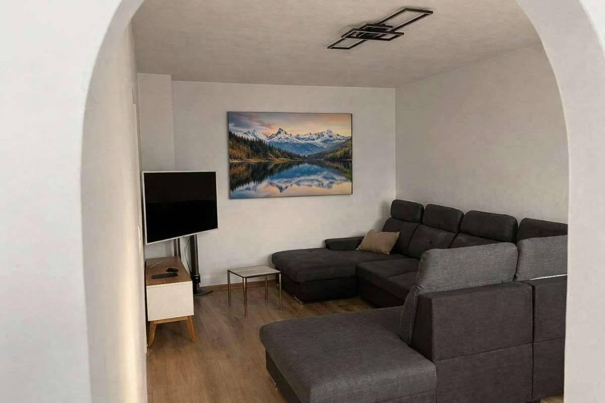 Gemütliches Wohnzimmer mit großem Ecksofa, Fernseher und einem Bild mit Berglandschaft.