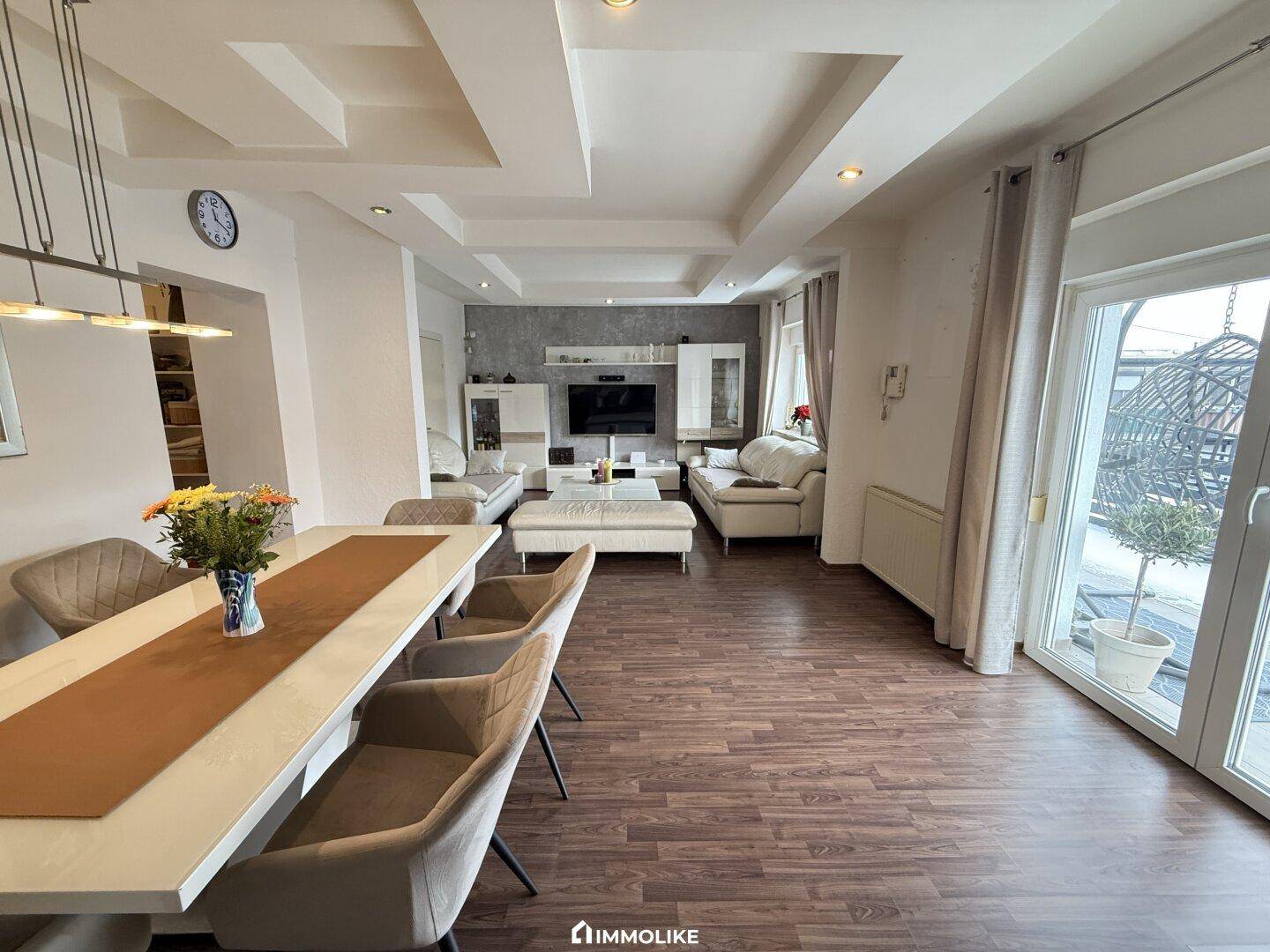 Heller, offener Wohn-Essbereich mit modernem Laminatboden und Zugang zum Balkon.