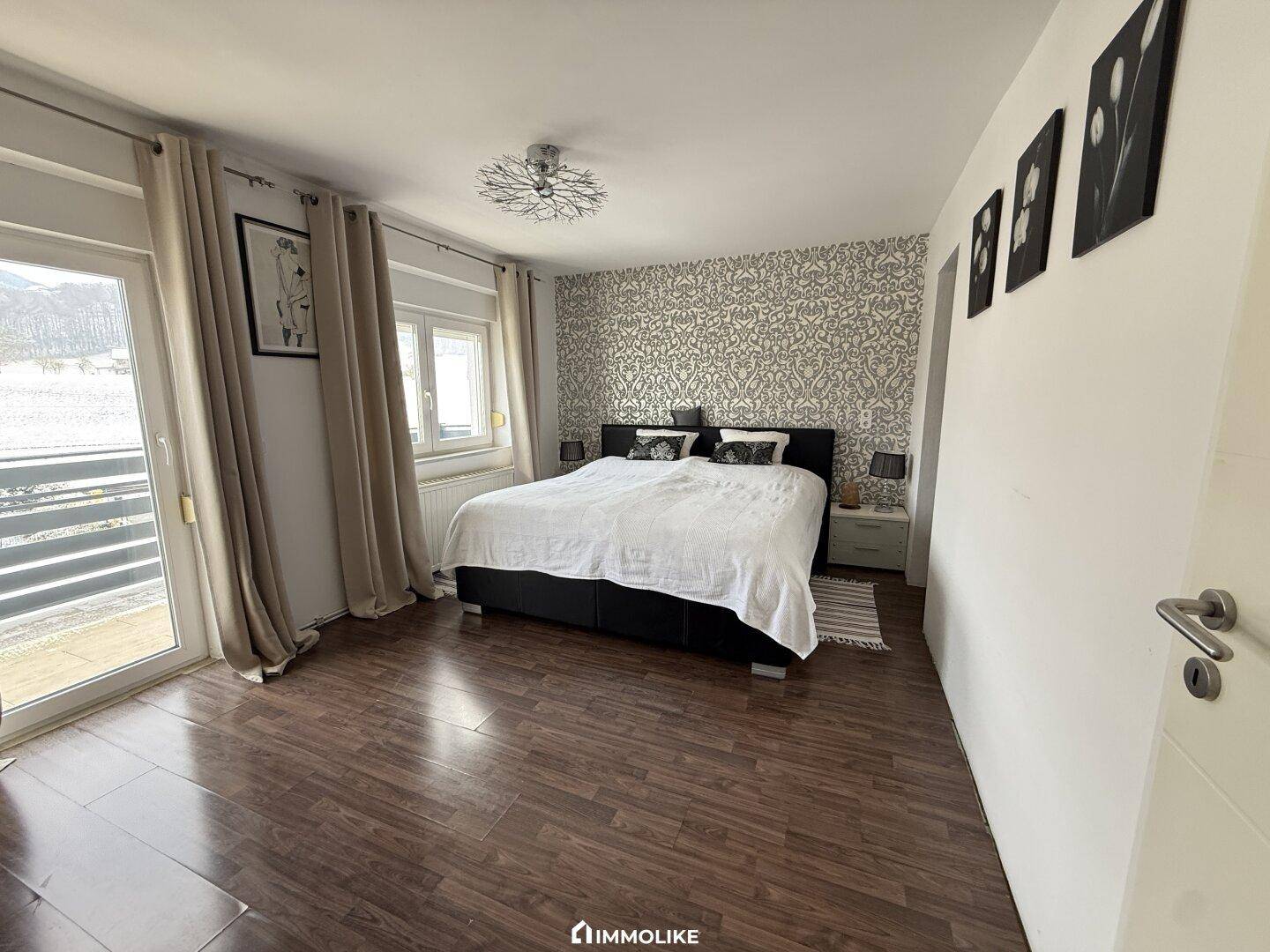 Gemütliches Schlafzimmer mit modernem Muster an der Wand und Balkonzugang.