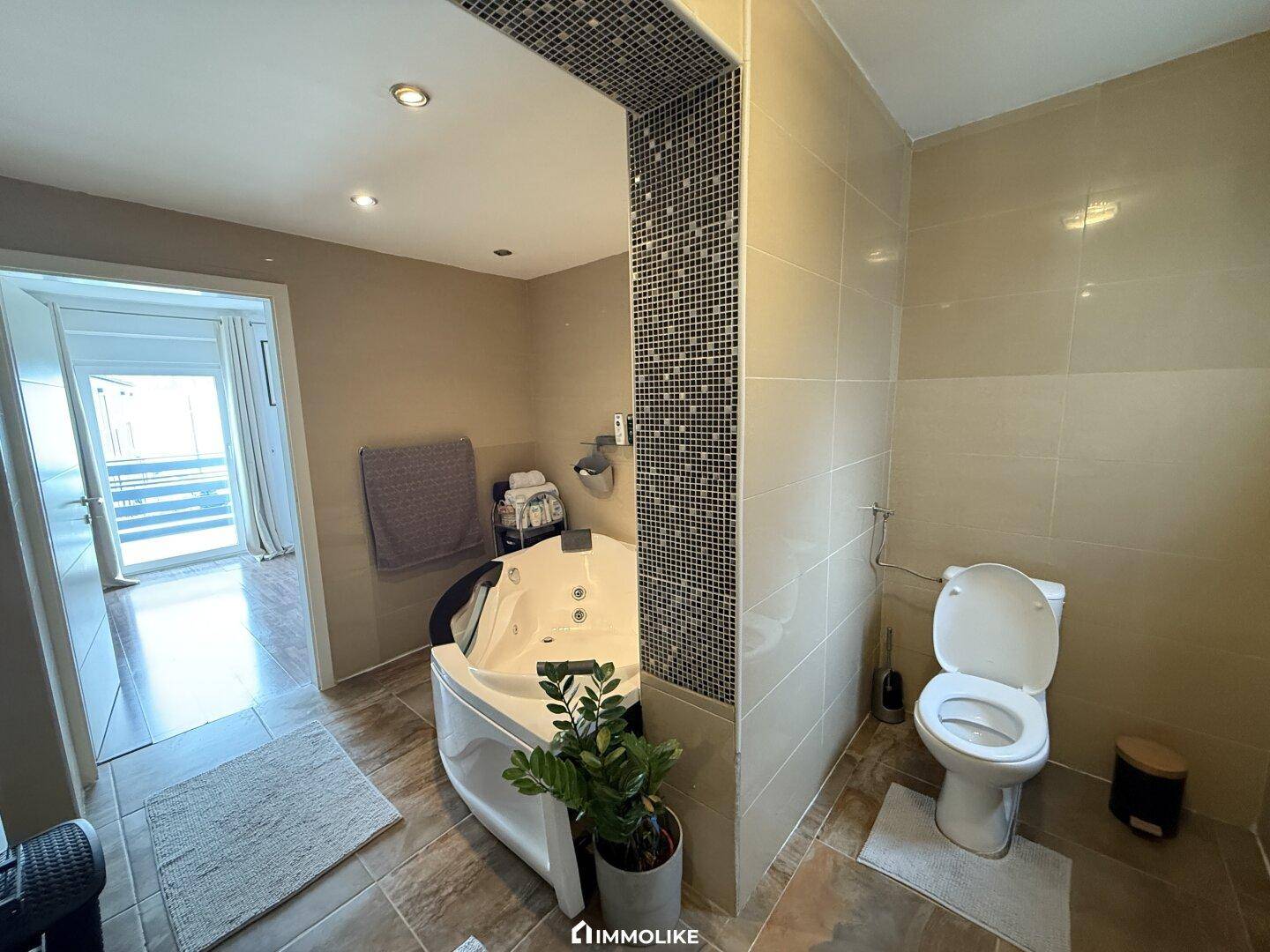 Badezimmer mit Eck-Whirlpool, Toilette und Zugang zu einem weiteren Raum.