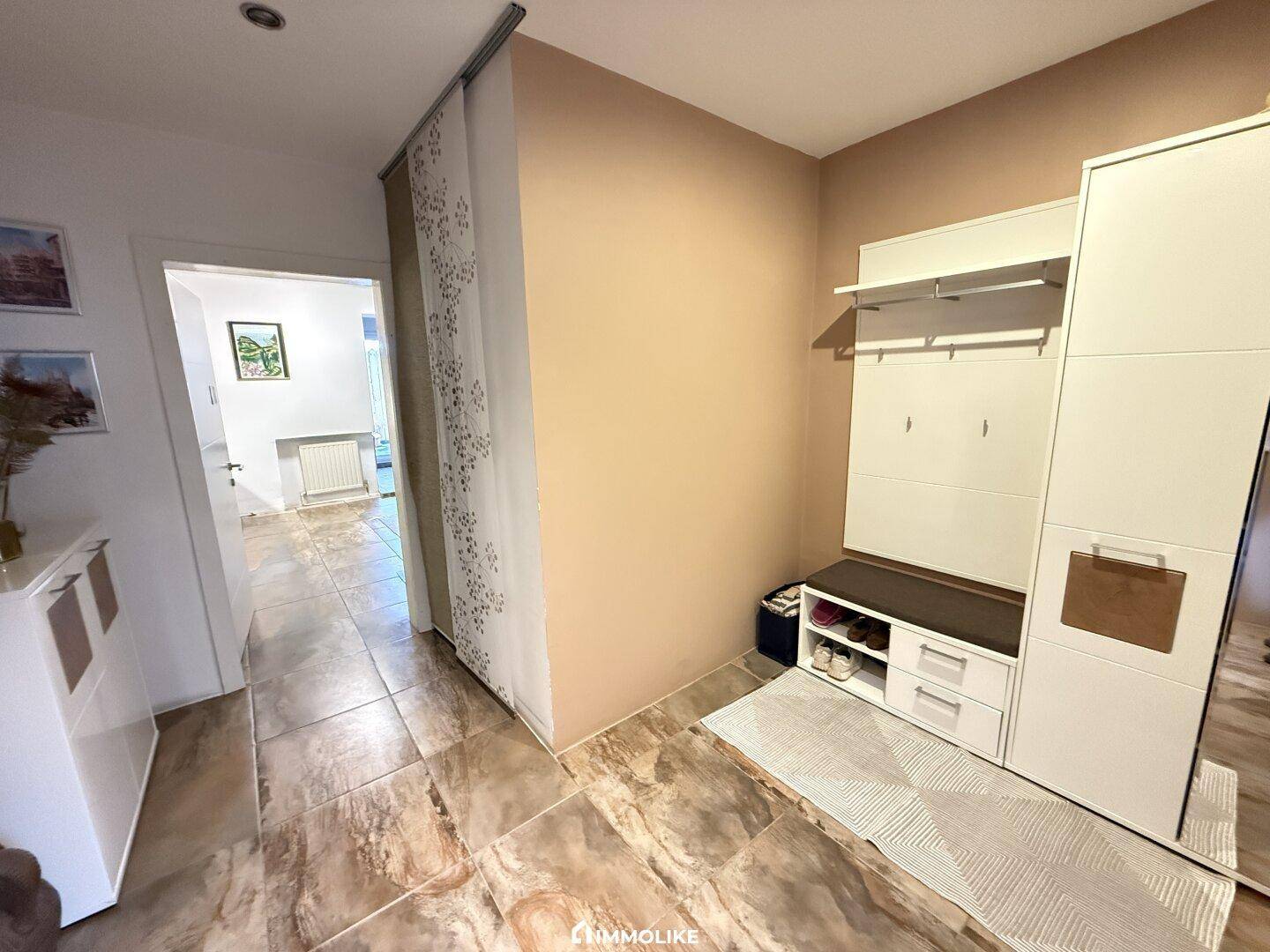 Eingangsbereich mit Fliesenboden und Garderobe, der zu weiteren Räumen führt.