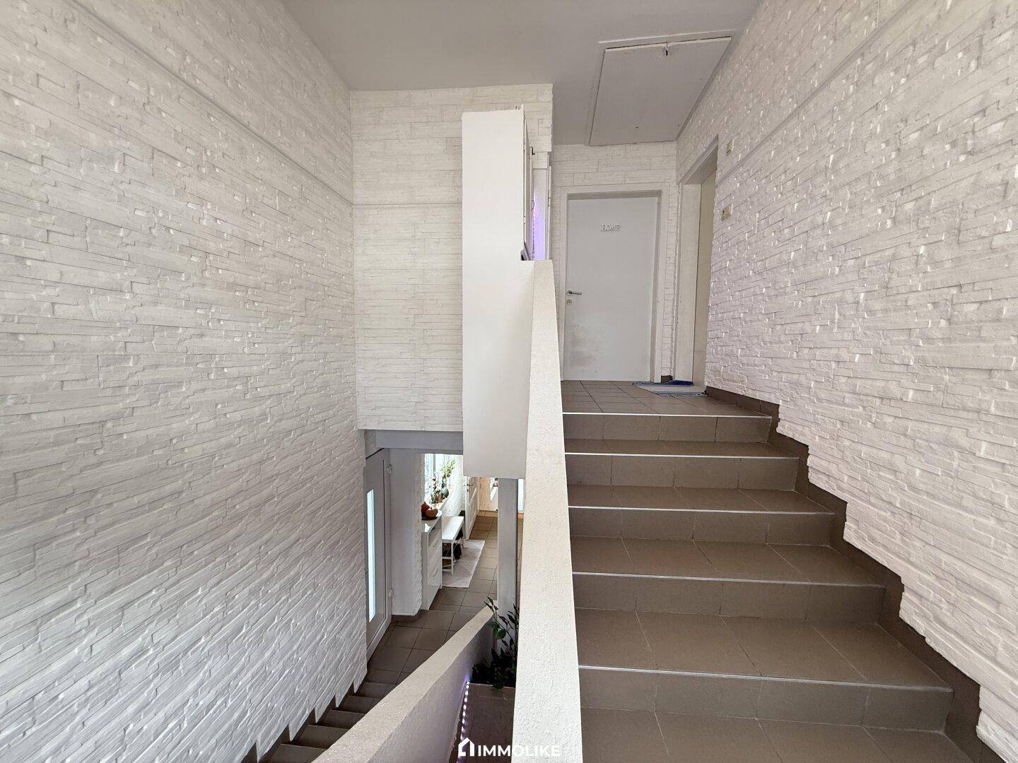 Treppenhaus mit strukturierten weißen Wänden und Fliesenboden.