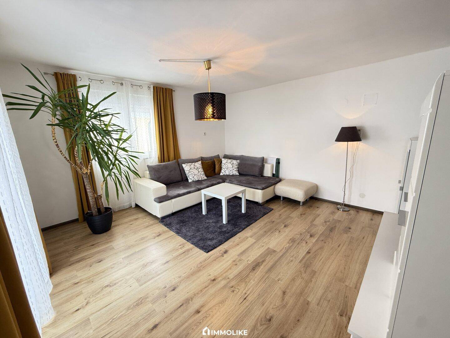 Gemütliches Wohnzimmer mit Laminatboden, großem Sofa und gelben Vorhängen.
