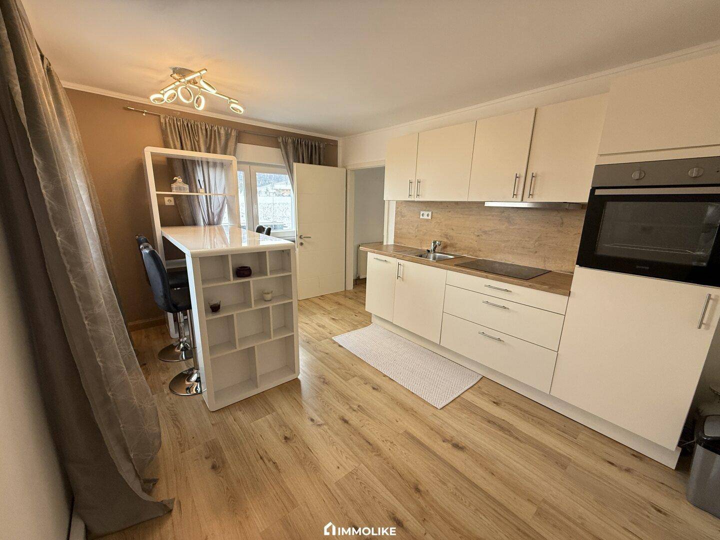 Helle Küche mit weißer Einbauküche, Frühstücksbar und Laminatboden.