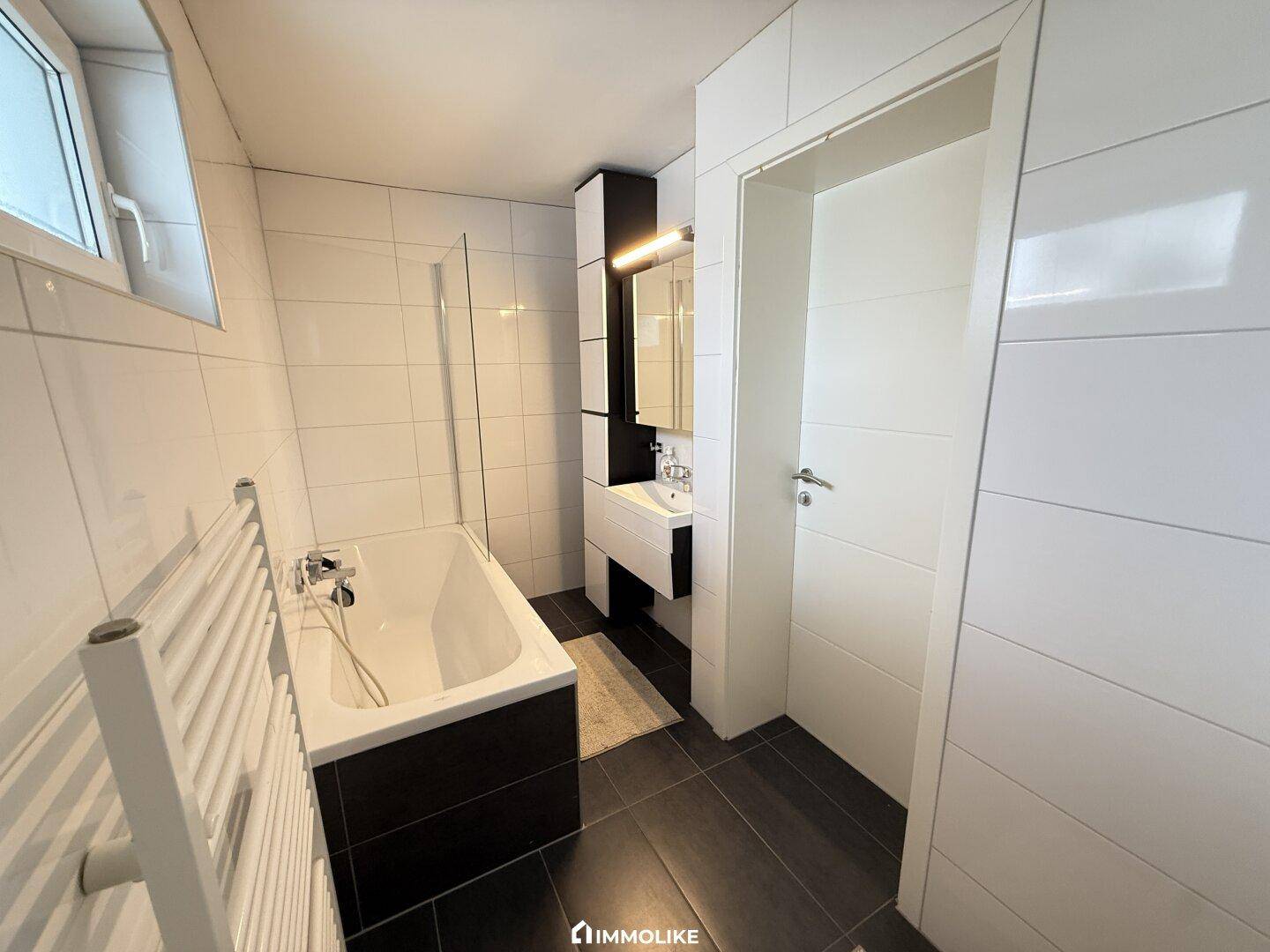 Modernes Badezimmer mit Badewanne, Duschabtrennung und beheiztem Handtuchhalter.