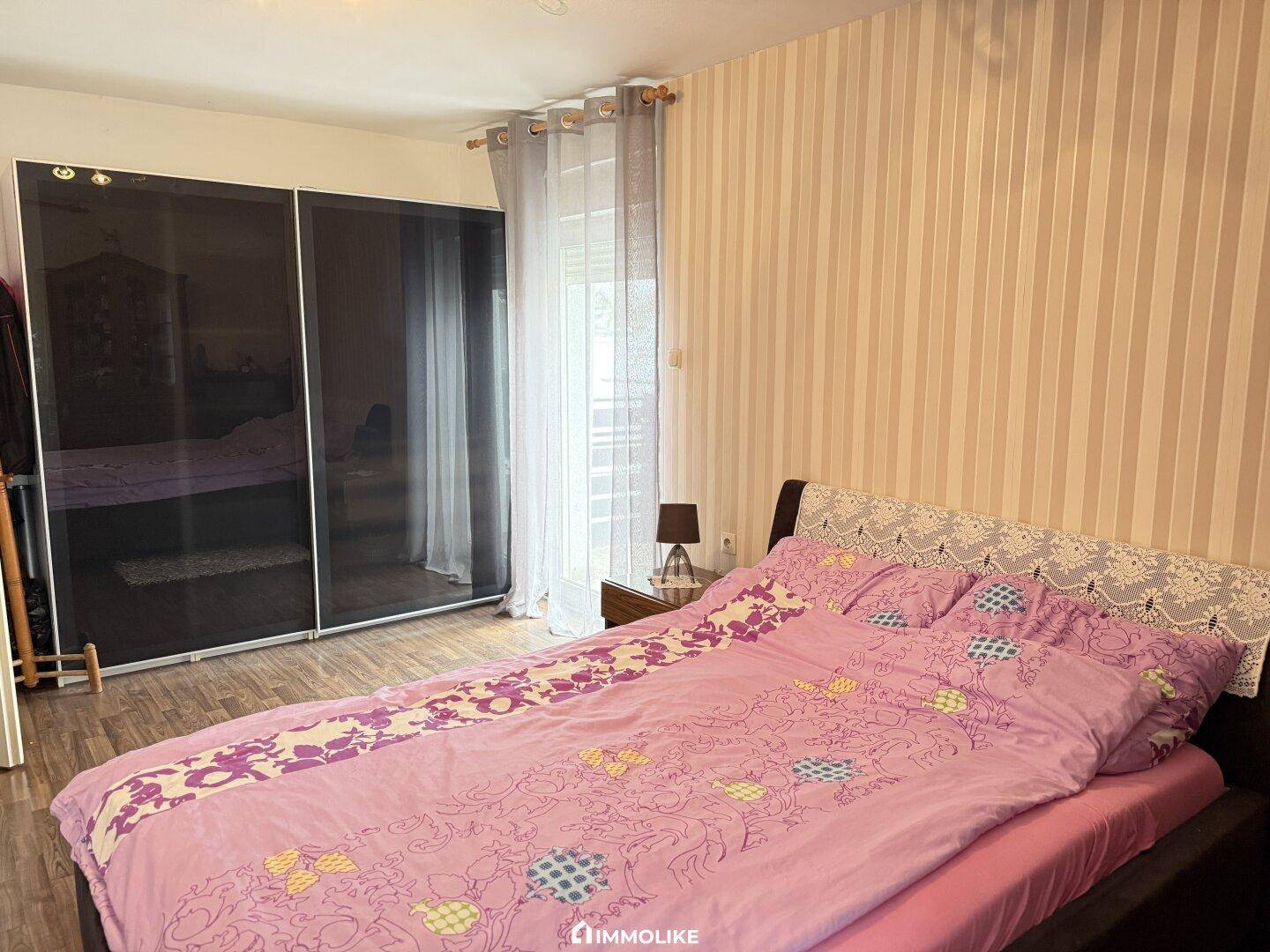 Schlafzimmer mit Doppelbett, gemusterter Tapete und großem Schiebetürenschrank.