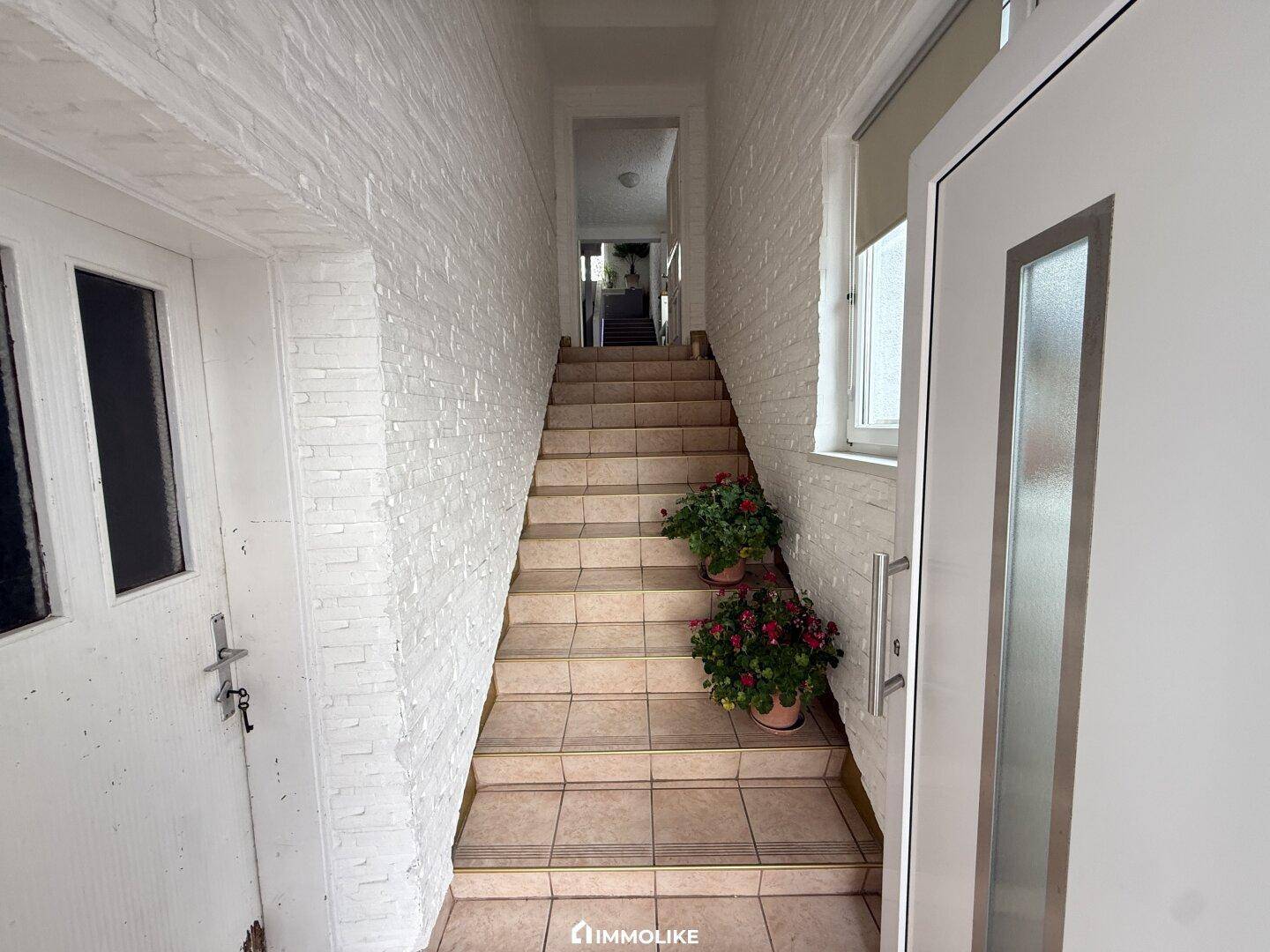 Eingangsbereich mit gefliesten Treppen und weiß gestrichenen Ziegelwänden.