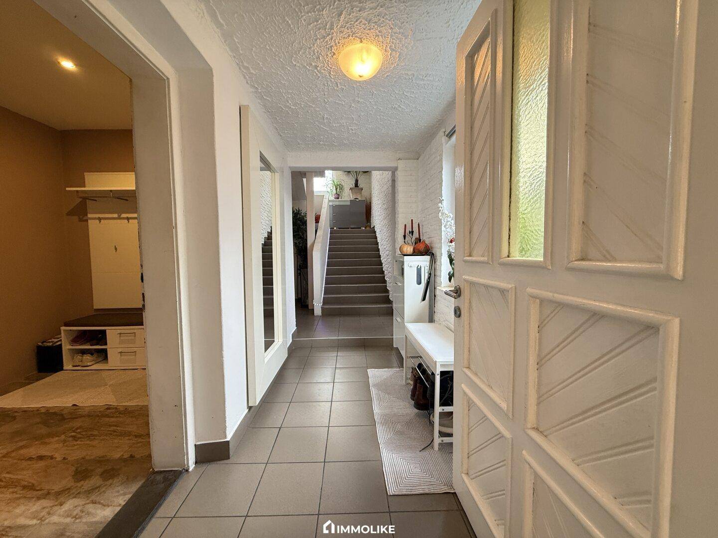 Heller Eingangsbereich mit Fliesenboden, Garderobe und Zugang zur Treppe.