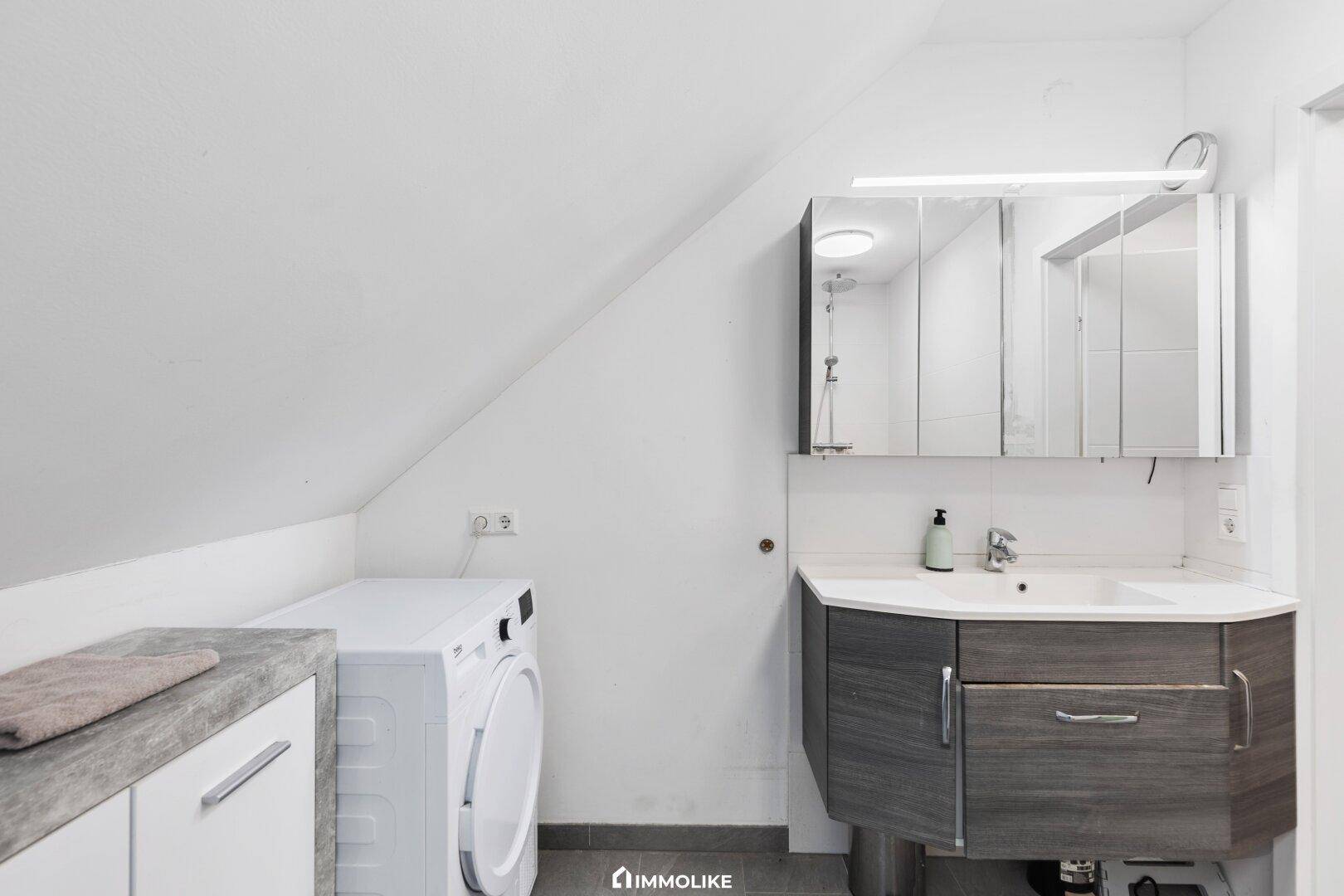 Modernes Badezimmer im Dachgeschoss mit Waschmaschine, Waschbecken und Spiegelschrank.