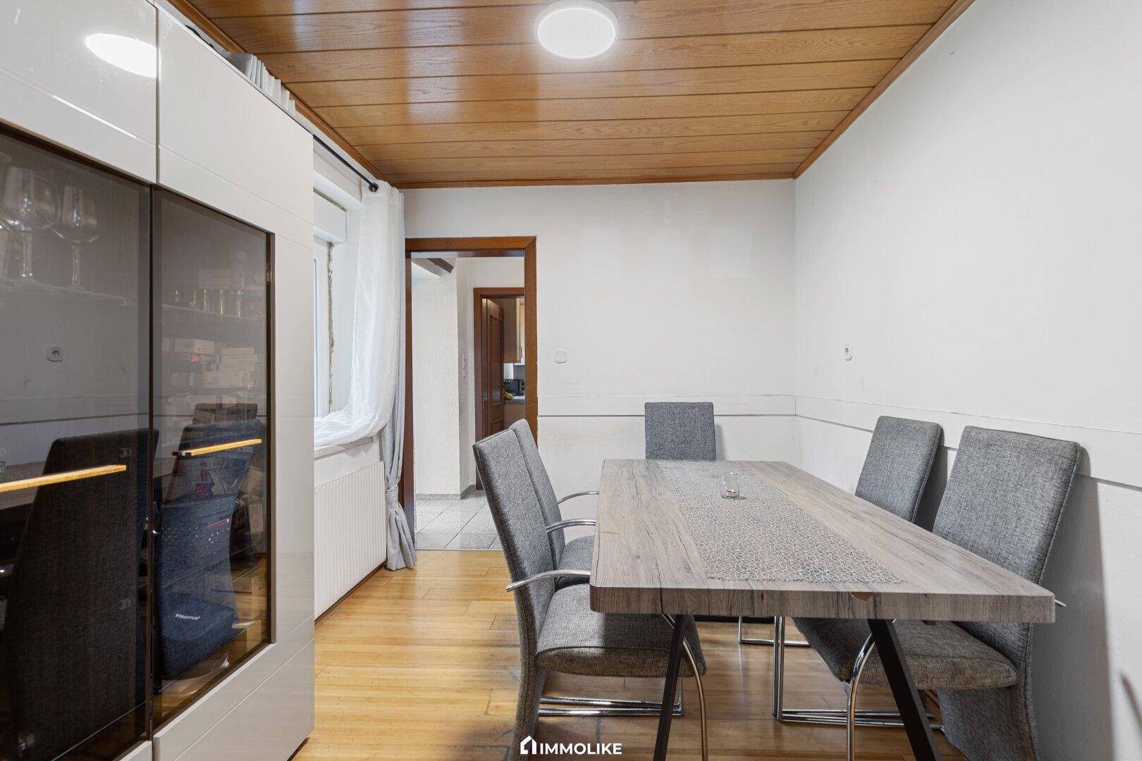 Esszimmer mit Holzboden, großem Esstisch und Holzdecke, verbunden mit dem Wohnbereich.