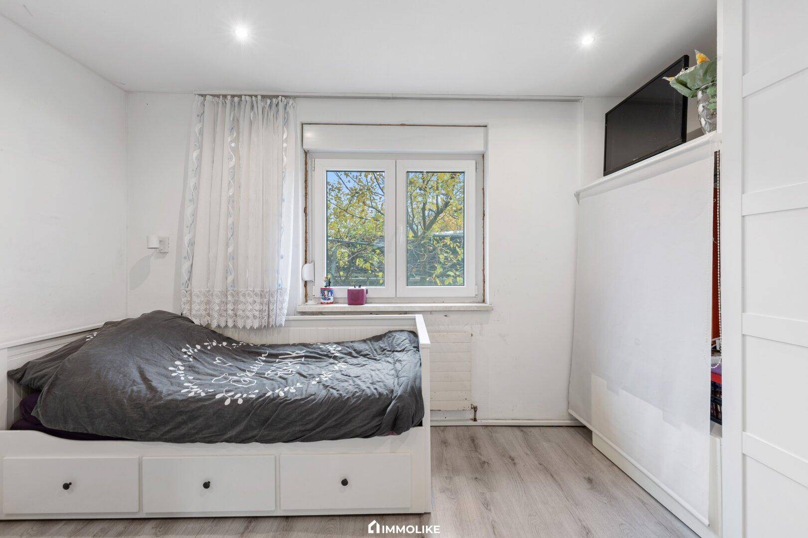 Schlafzimmer mit Einzelbett, Kleiderschrank und Fenster mit Blick ins Grüne.