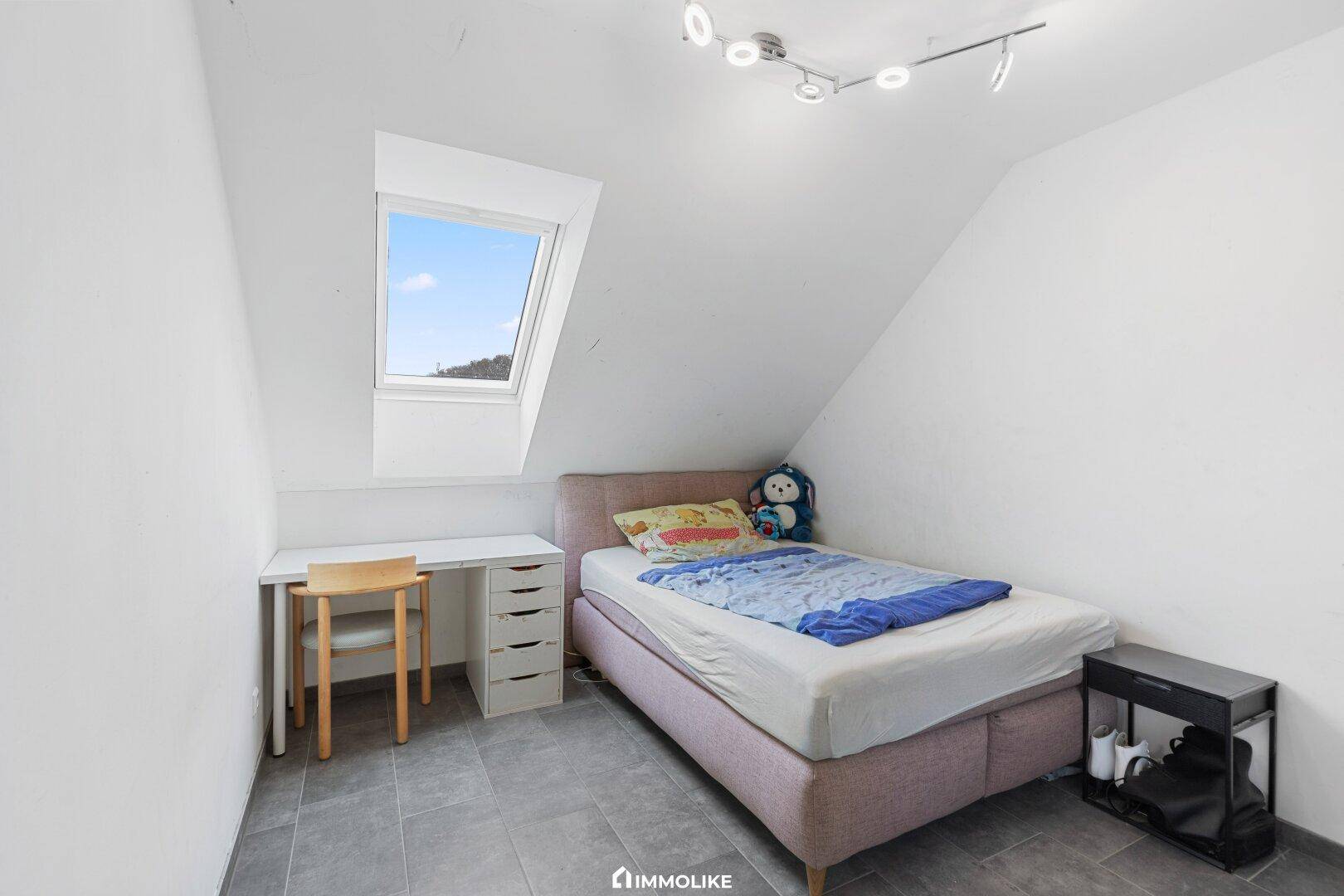 Helles Schlafzimmer im Dachgeschoss mit Einzelbett, Schreibtisch und Dachfenster.