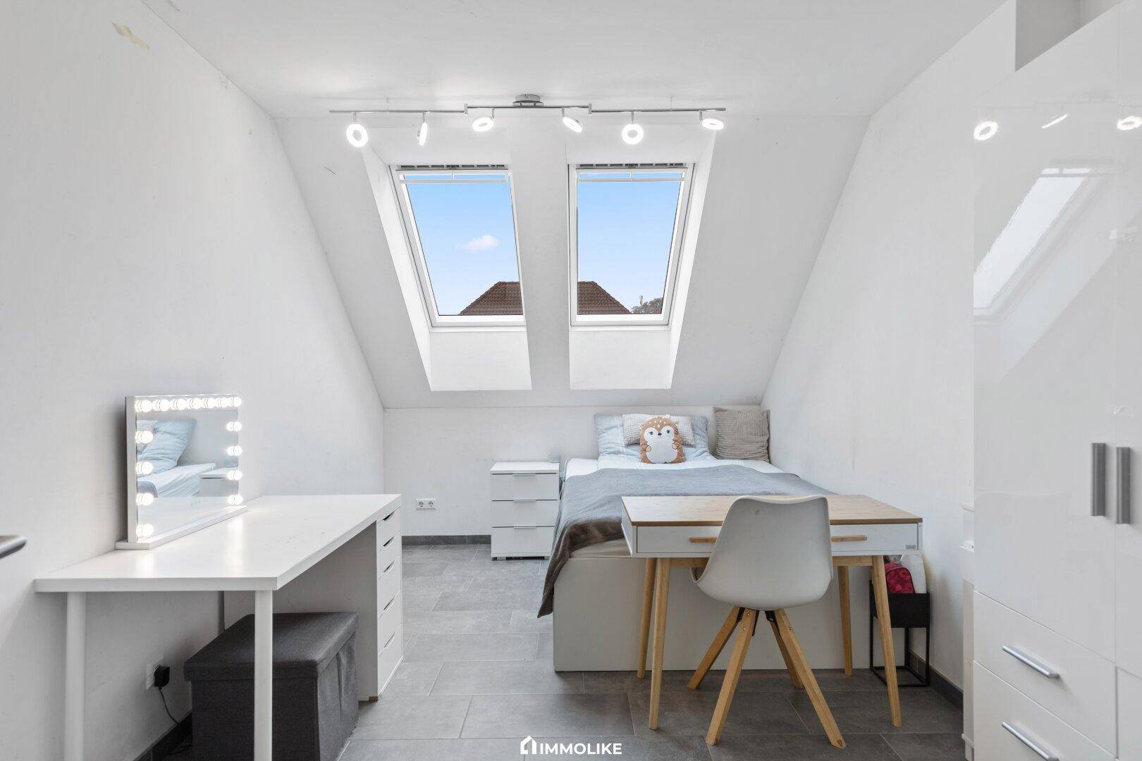 Geräumiges Schlafzimmer im Dachgeschoss mit zwei Dachfenstern, Bett und Schreibtisch.