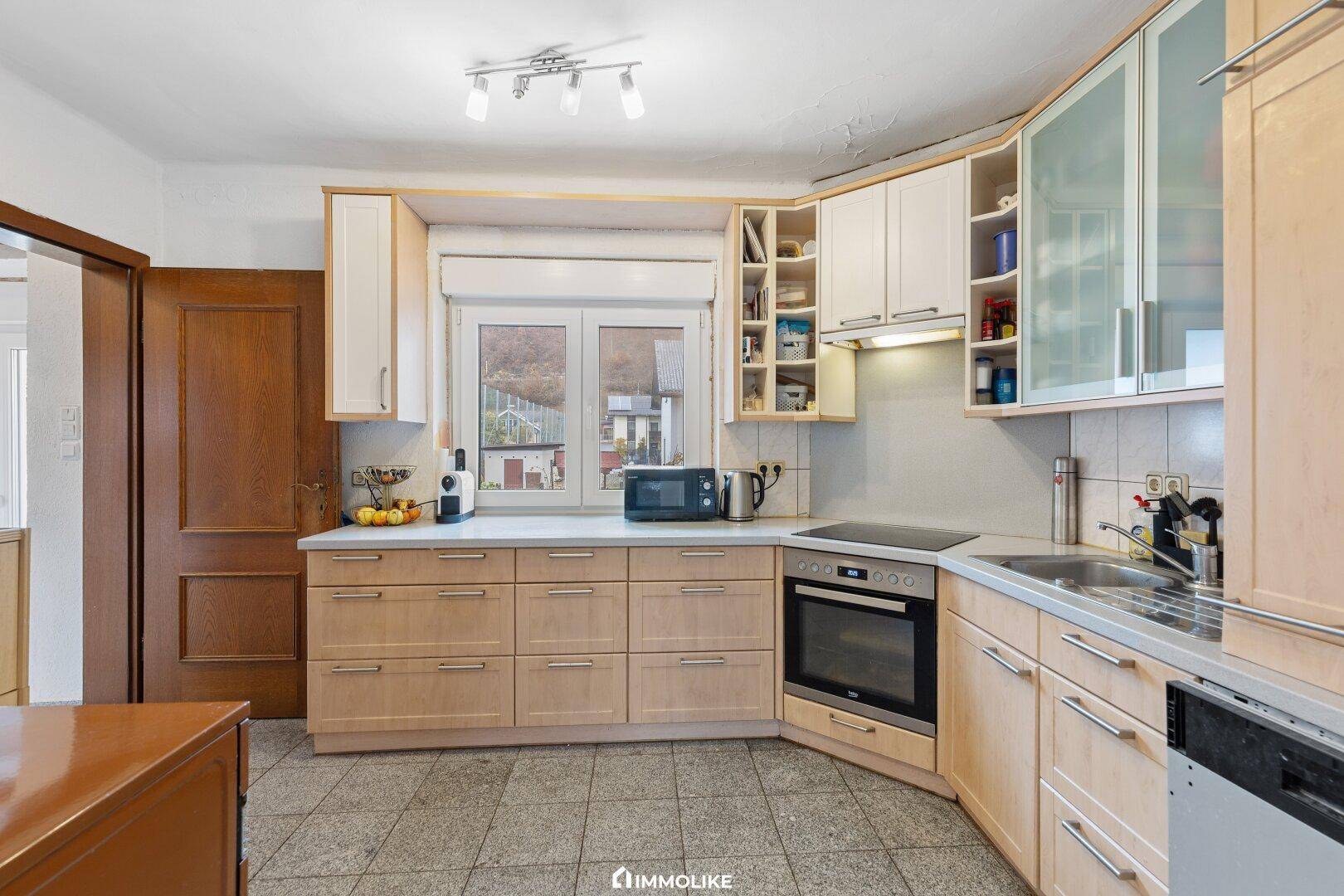Funktionale Küche mit Holzschränken, Einbaugeräten und Fenster mit Blick nach draußen.