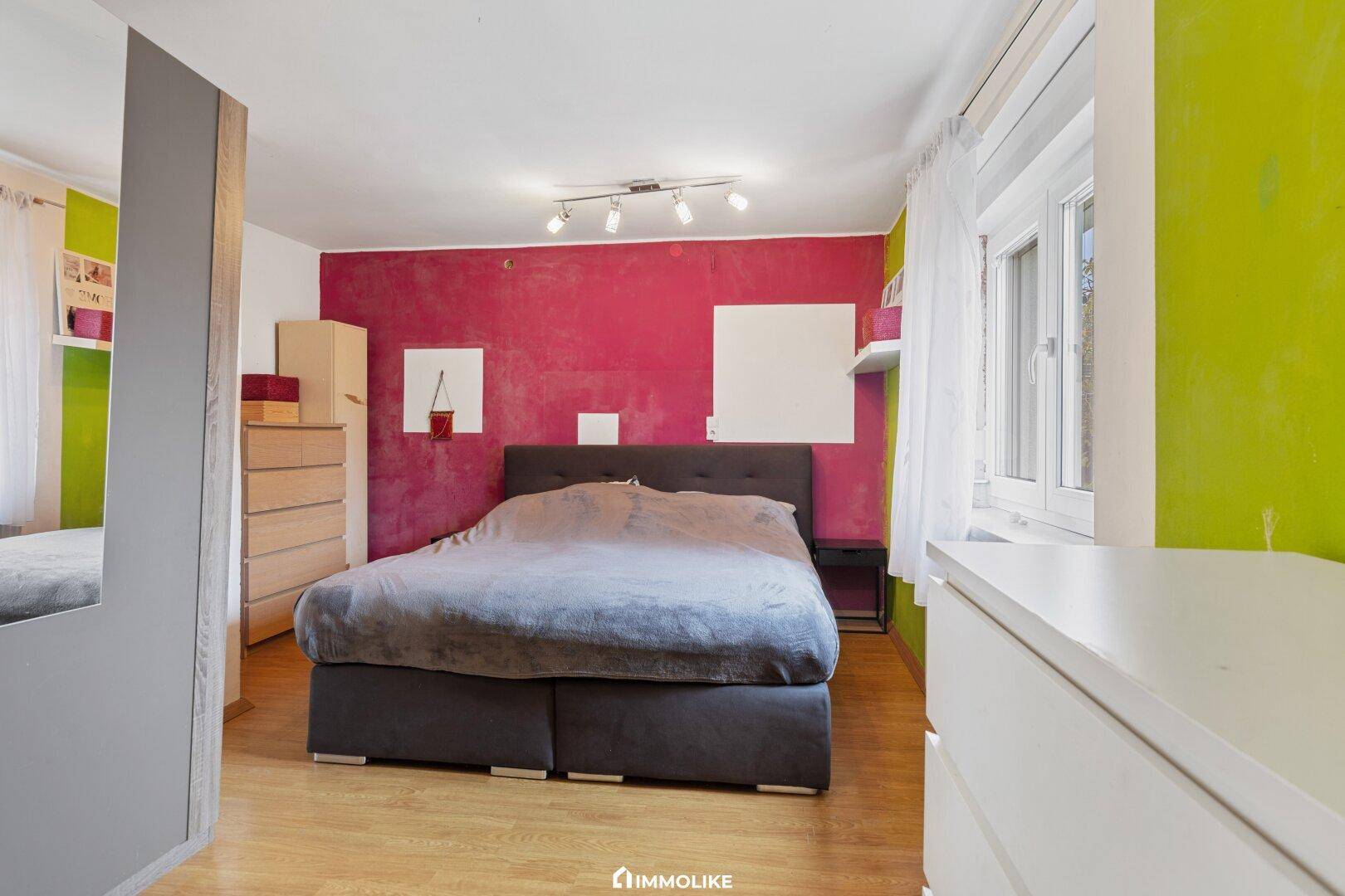 Schlafzimmer mit farbigen Wänden, Doppelbett und Holzboden, bietet eine lebendige Atmosphäre.