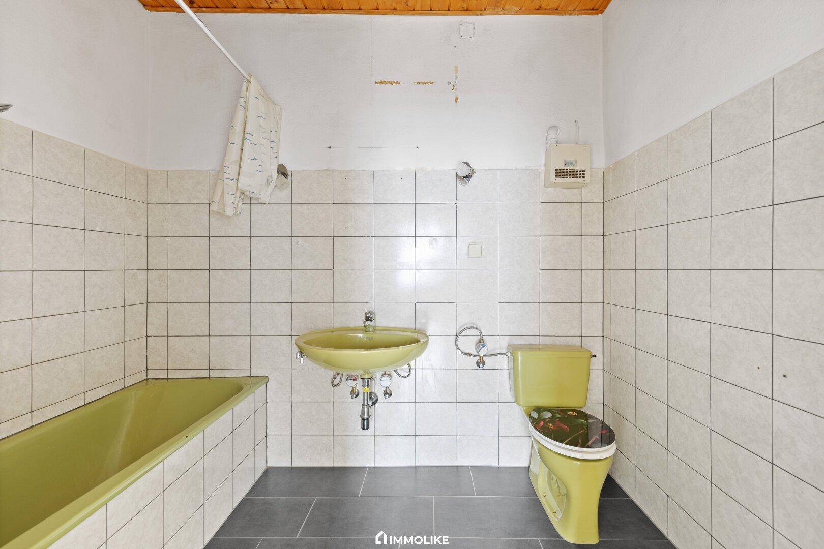 Badezimmer mit älteren Fliesen, einer Badewanne und einem WC in Lindgrün.