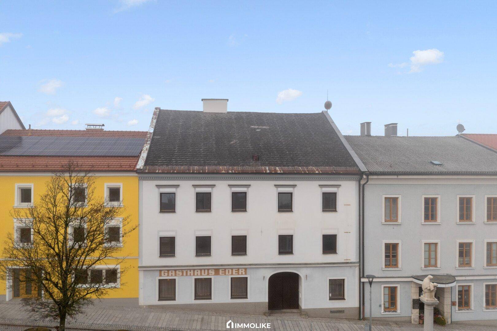 Frontansicht des Gasthauses Eder mit umliegenden Gebäuden und einem klaren Himmel.