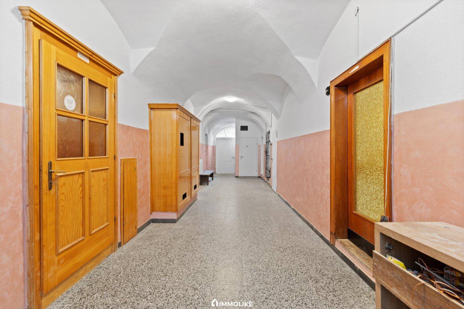 Langer Flur mit Terrazzoboden, Holztüren und gewölbter Decke in einem historischen Gebäude.