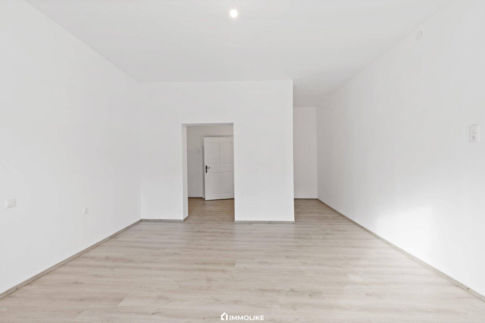 Geräumiger, leerer Raum mit Laminatboden und weiß gestrichenen Wänden, bereit zur Gestaltung.