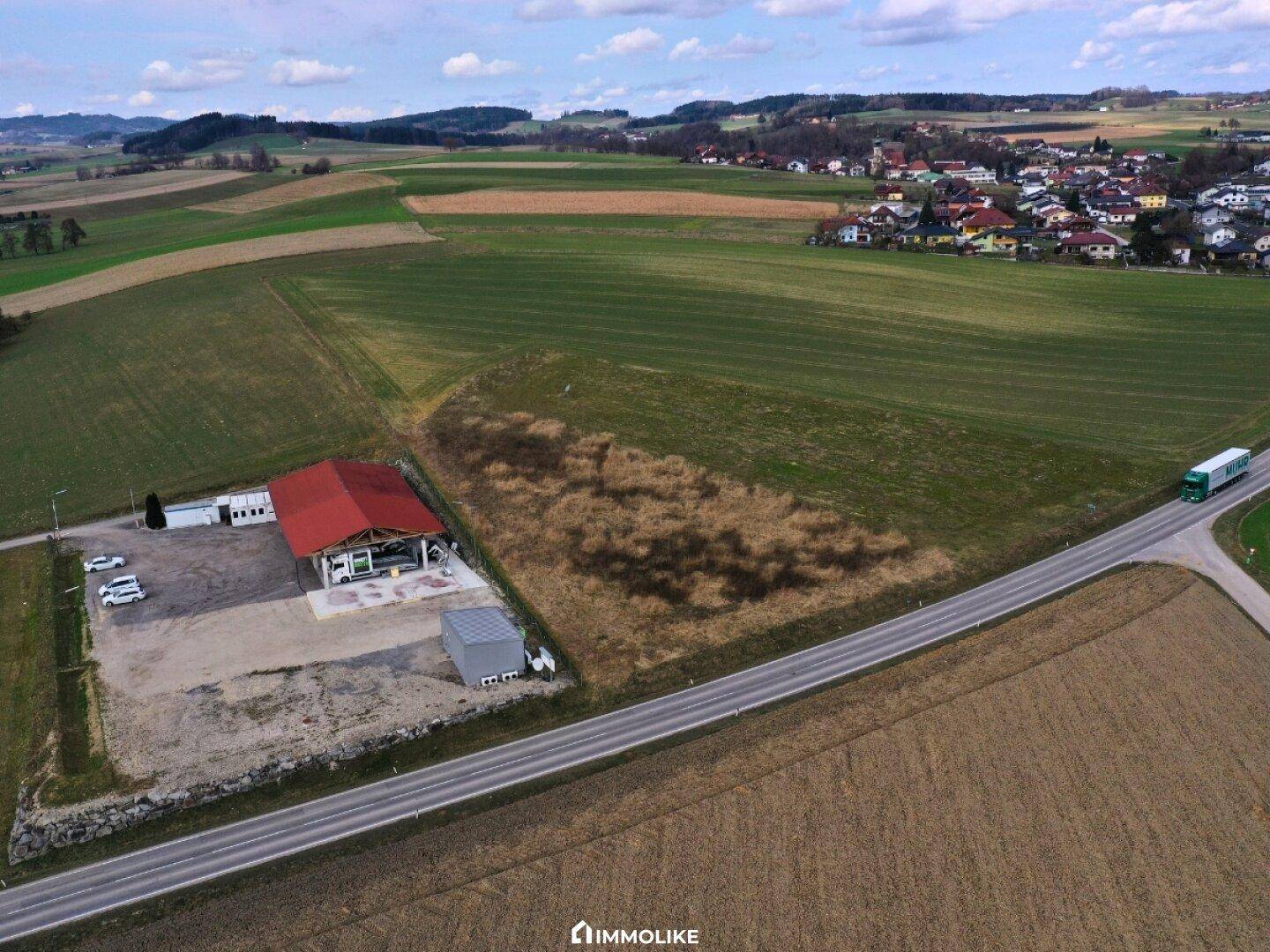 Weitläufige Luftaufnahme des Anwesens mit rotem Dach, umgeben von grünen Feldern, einer Straße und einem entfernten Dorf.