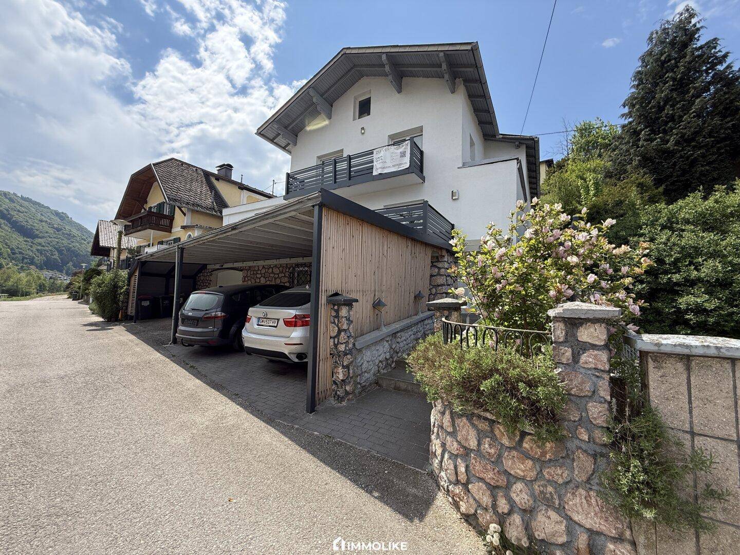 Ansicht des weißen Wohnhauses mit Carport und gepflegter Steinfassade im unteren Bereich des Gebäudes.