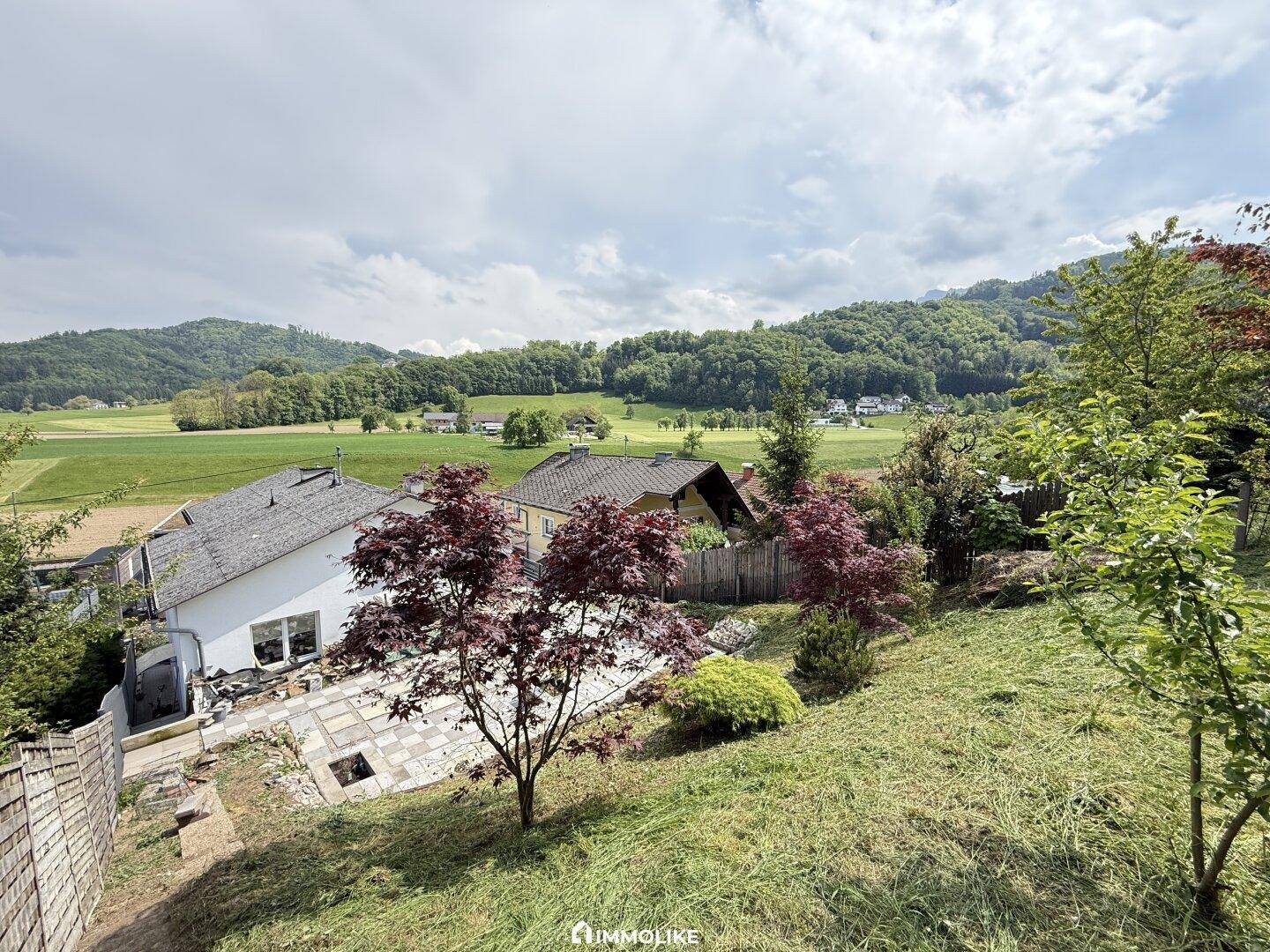 Weitläufiger Blick auf das Anwesen mit Terrasse, Garten und die umliegende grüne Landschaft und Hügel.