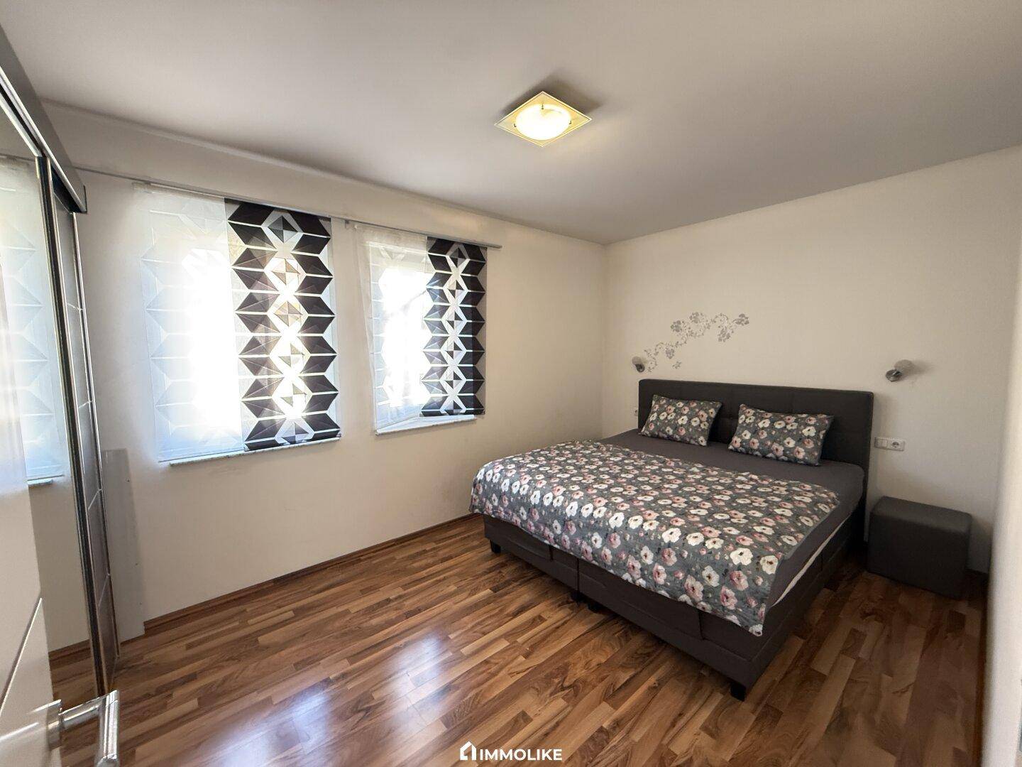 Gemütliches Schlafzimmer mit Doppelbett, Holzfußboden und großen Fenstern für viel Tageslicht.