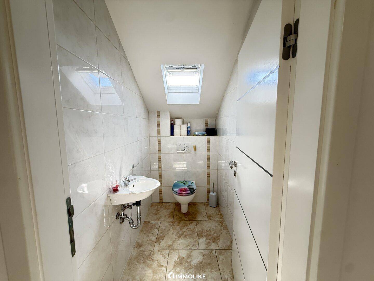 Kleines Gäste-WC mit Dachfenster, Waschbecken und hellen Fliesen.