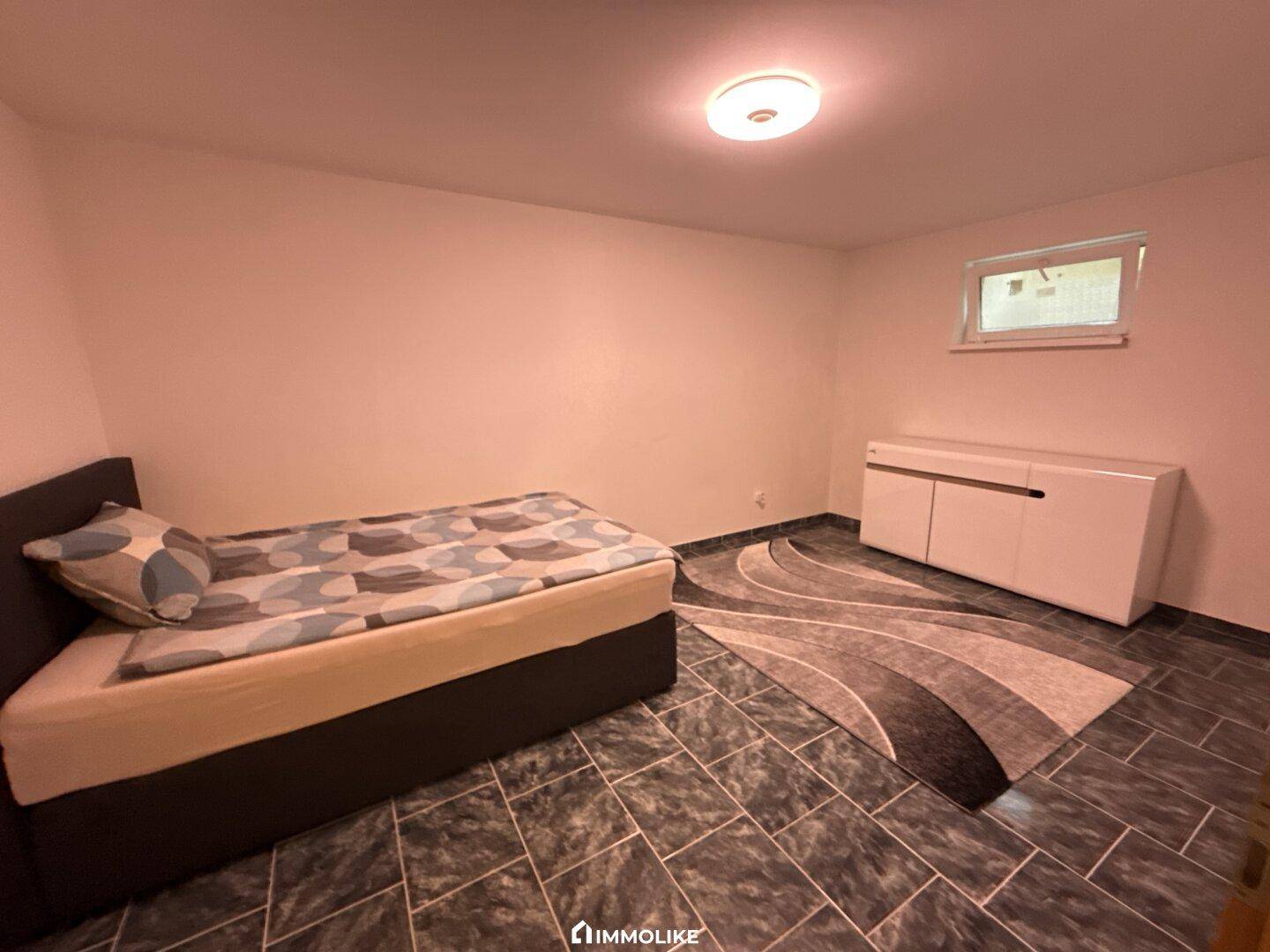 Schlafzimmer im Kellergeschoss mit Bett, Teppich und kleinem Fenster.